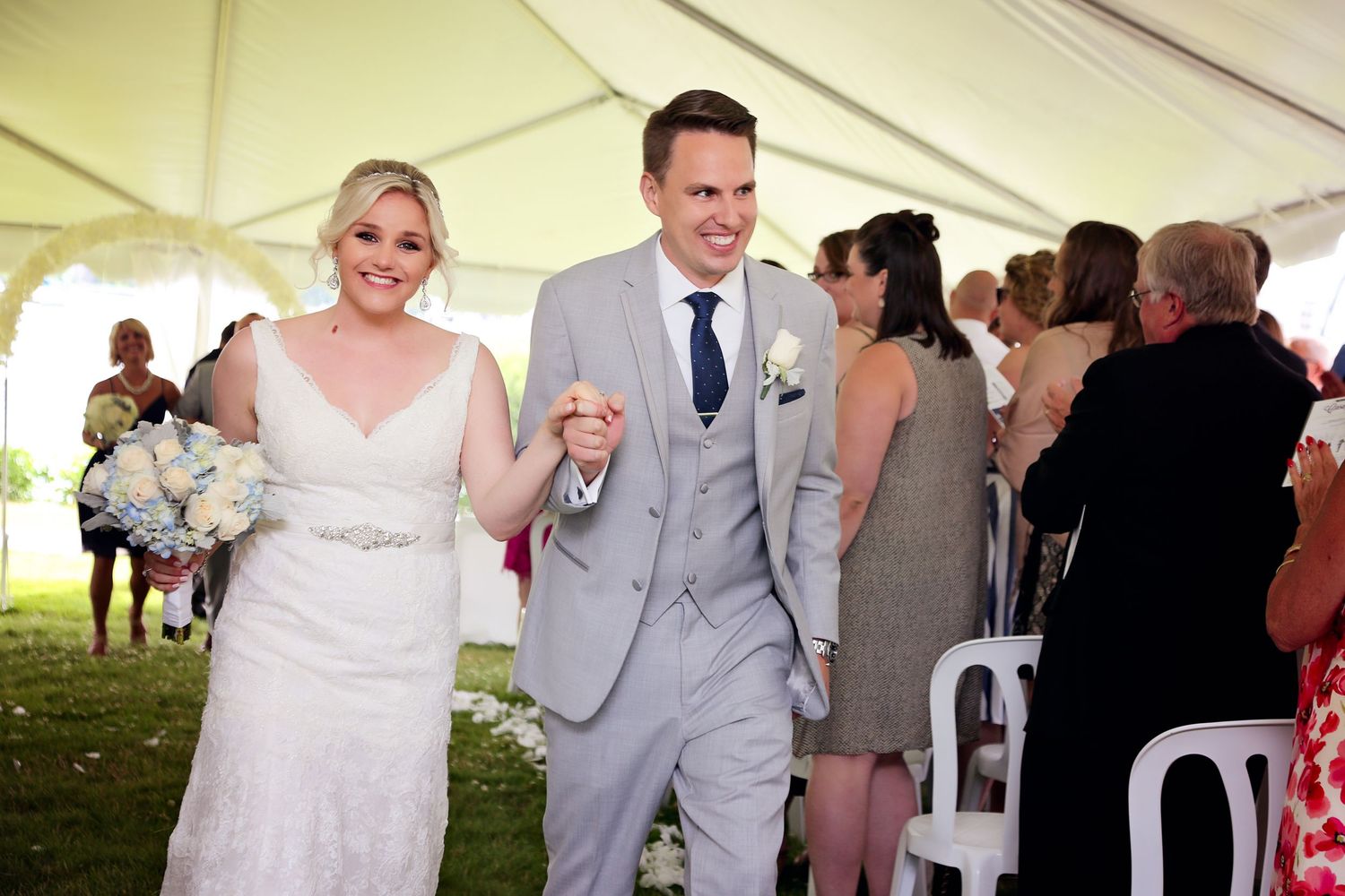 Wedding guests dance and celebrate together under a white tent at an outdoor reception.