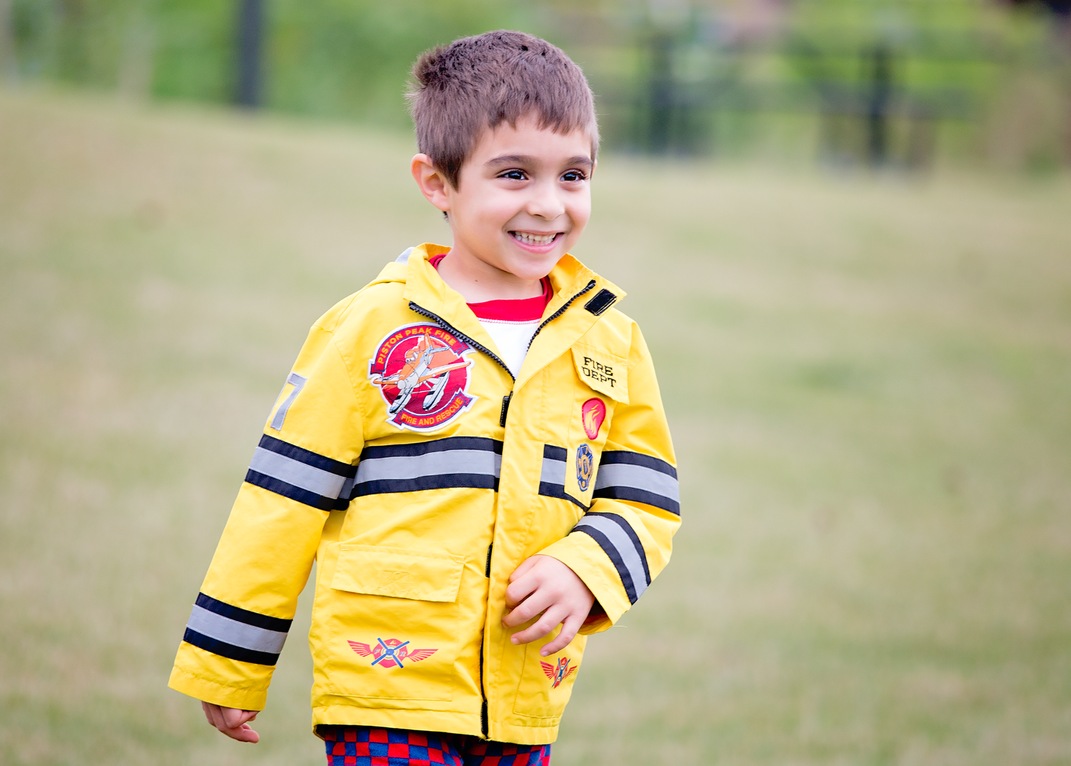A smiling figure in a bright yellow raincoat and rubber boots plays outdoors on a sunny autumn day.