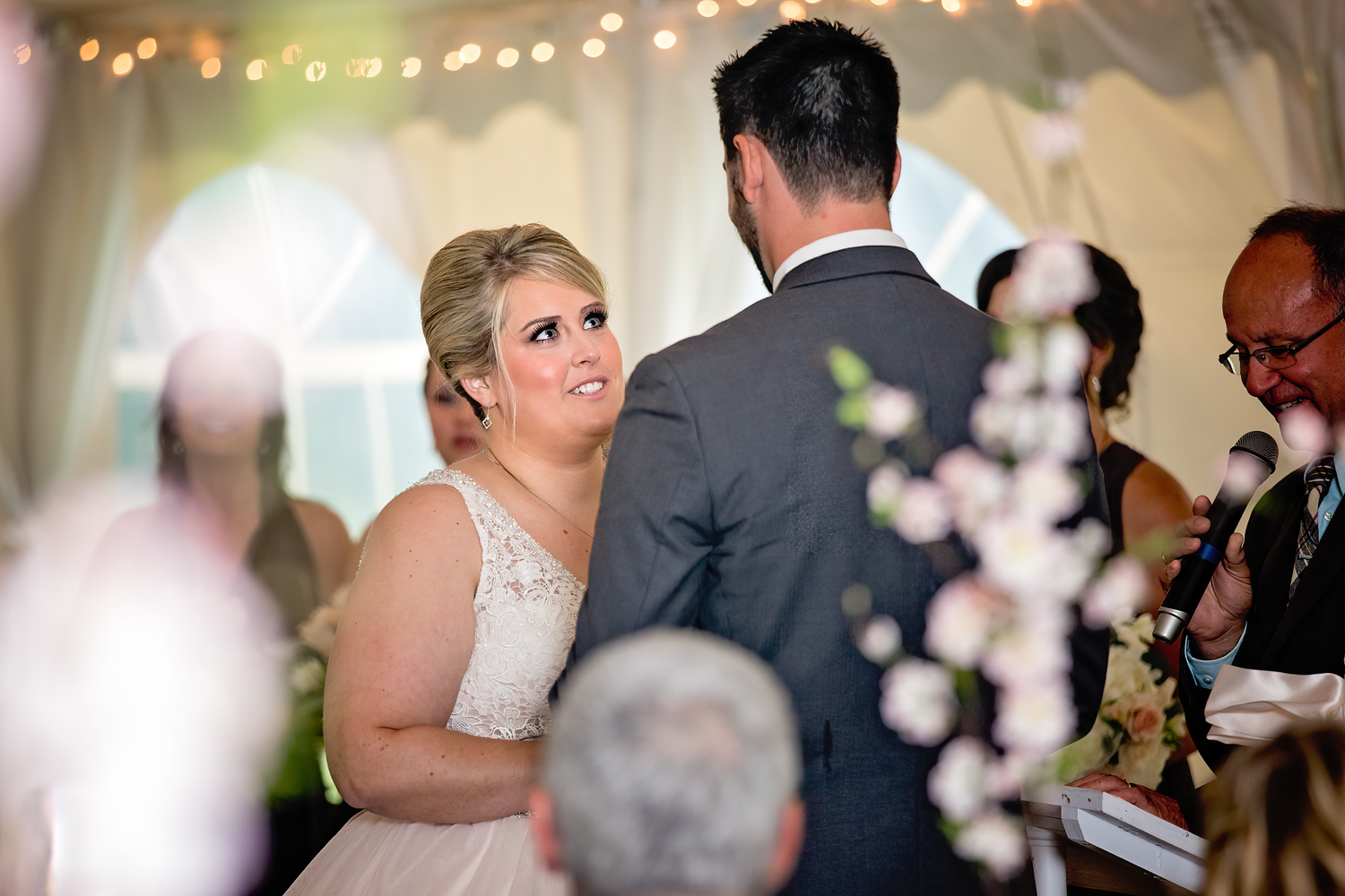 Wedding guests dance and celebrate under glowing string lights at an evening reception.