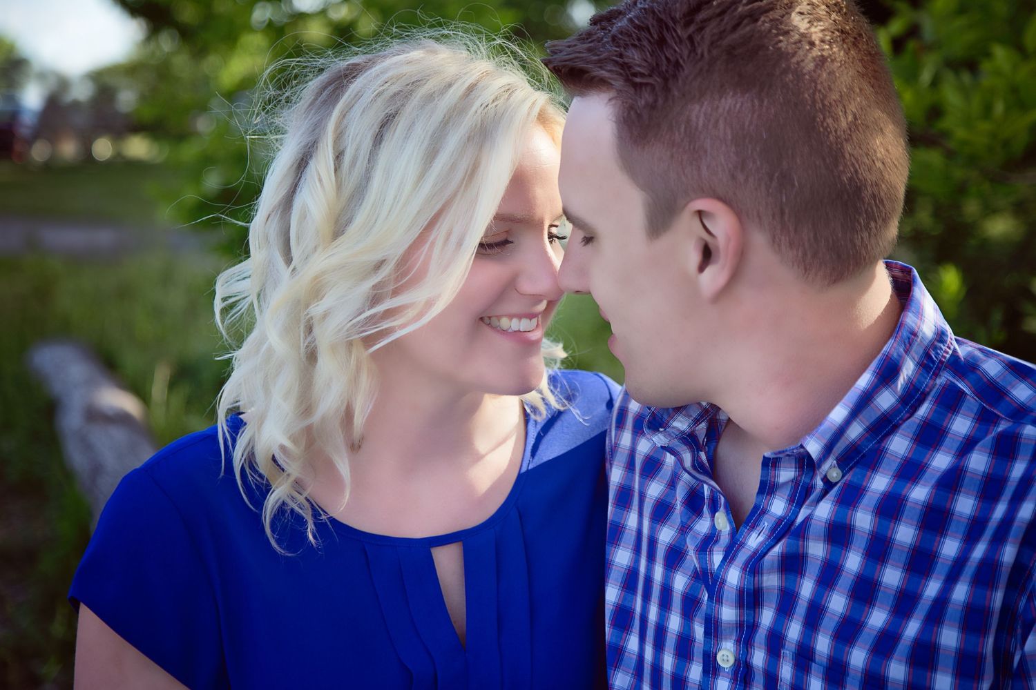 A couple in blue and white outfits share intimate moments during an outdoor photo session in a park setting.