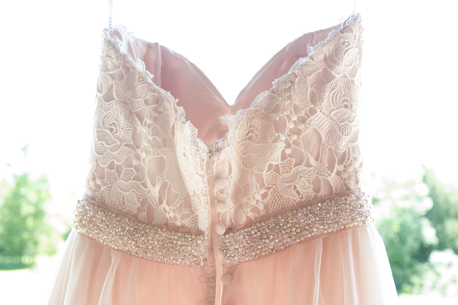 A row of blush pink bridesmaid dresses hanging on wooden hangers against a white wall.