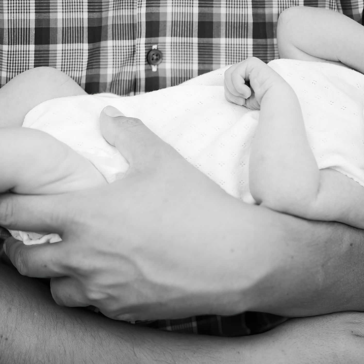 Black and white image of tiny baby feet and hands on plaid fabric.