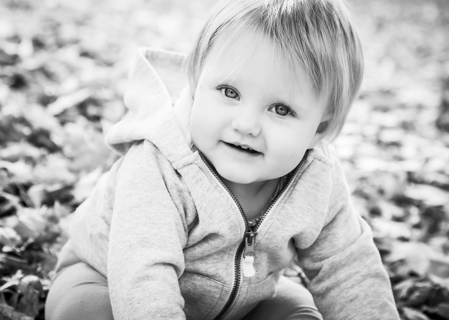 A series of black and white portraits showing a child playing in fallen autumn leaves.