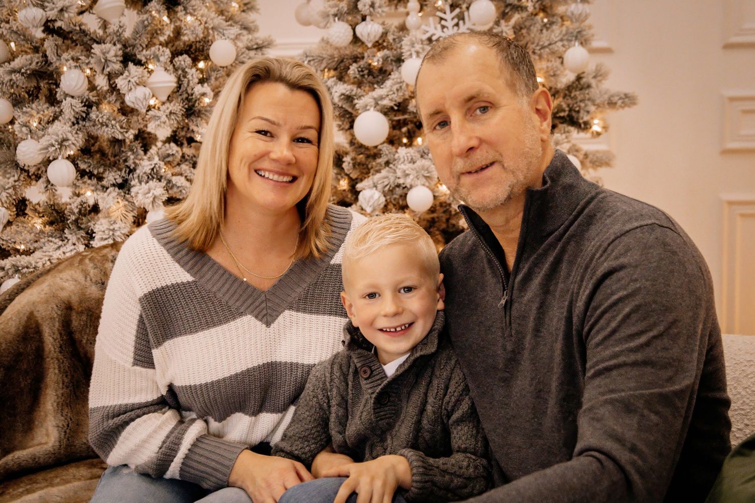 A family wearing cozy sweaters poses together in a warm-toned photo series with holiday decor in the background.