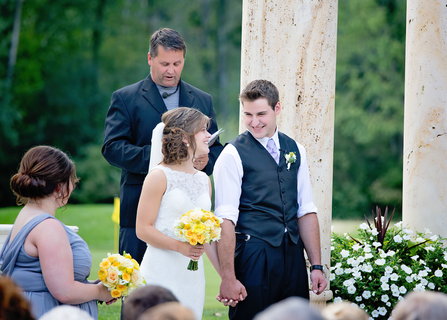 Wedding ceremony takes place outdoors with yellow bouquets and white floral arrangements creating a romantic atmosphere.