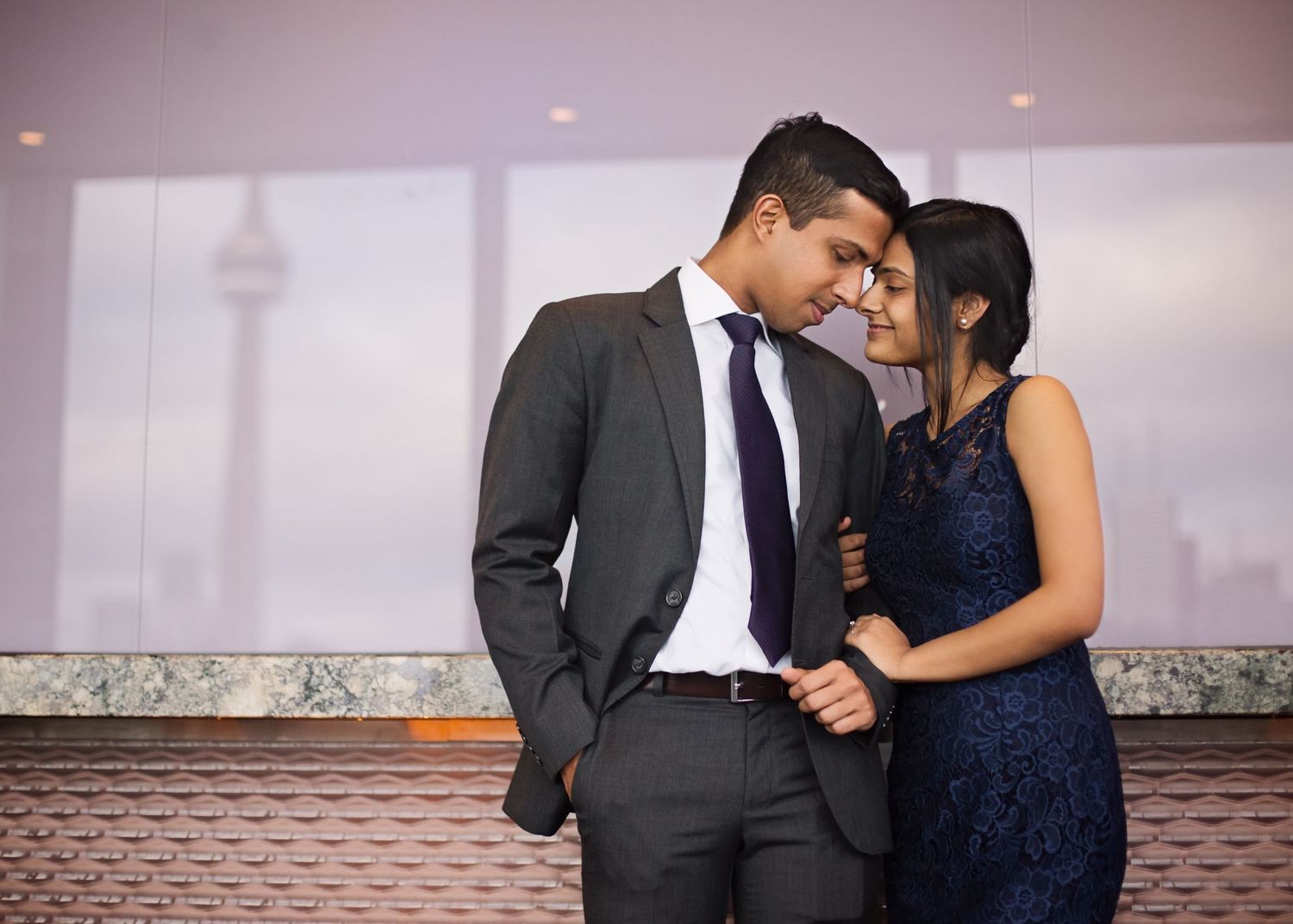 A couple in formal attire embraces during a romantic photoshoot against a soft blurred background.