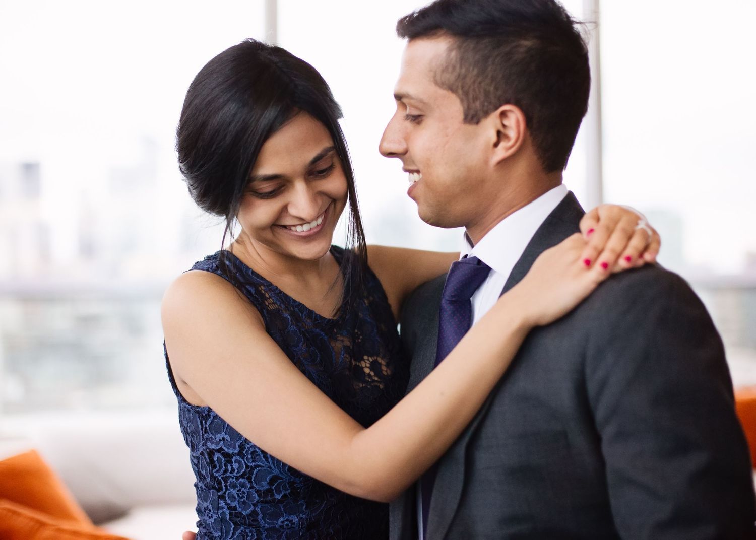 A couple in formal attire share an intimate moment together, with her in a navy dress and him in a dark suit.