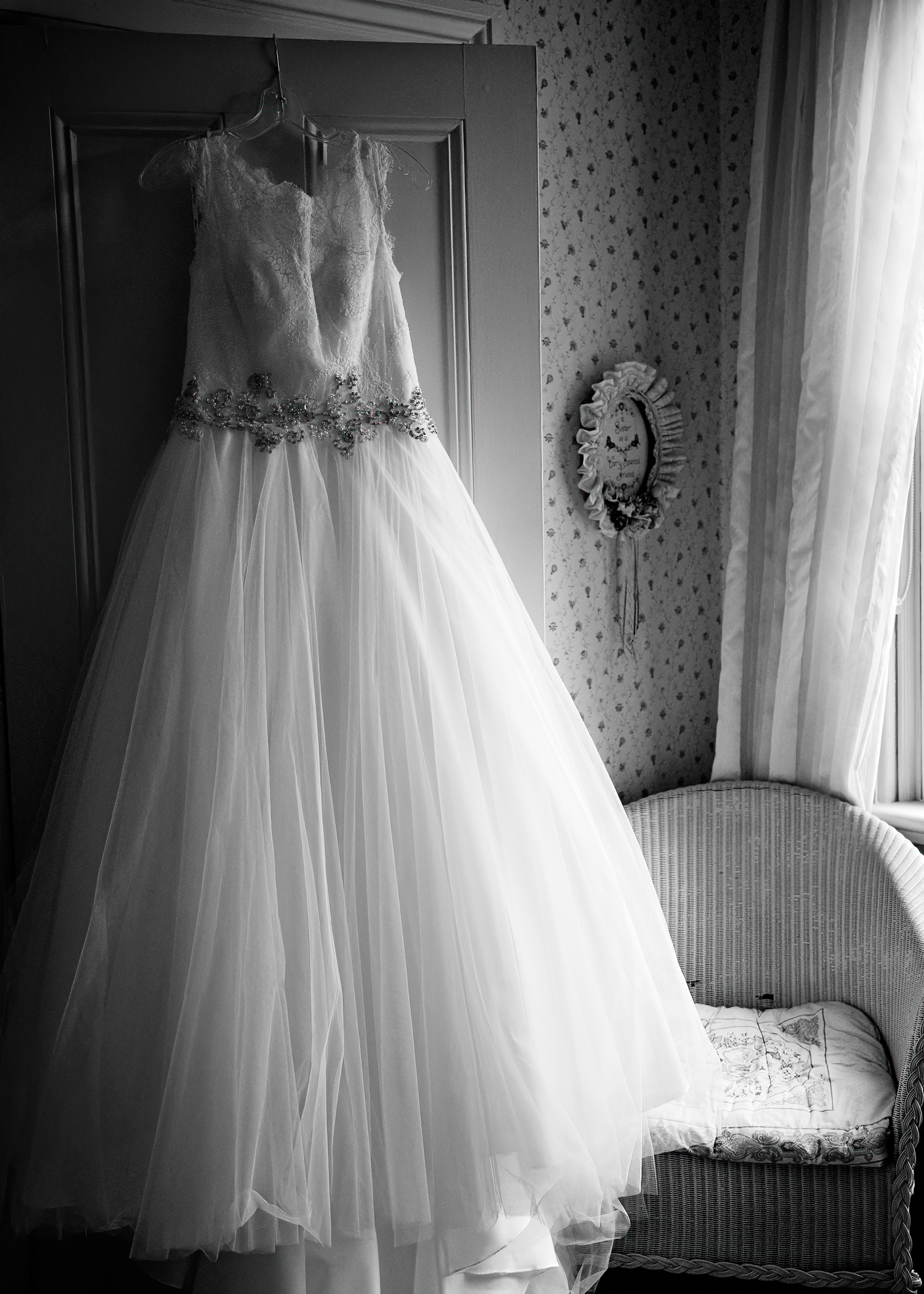 A series of black and white photographs showing a white tulle wedding dress displayed in different angles by a window.