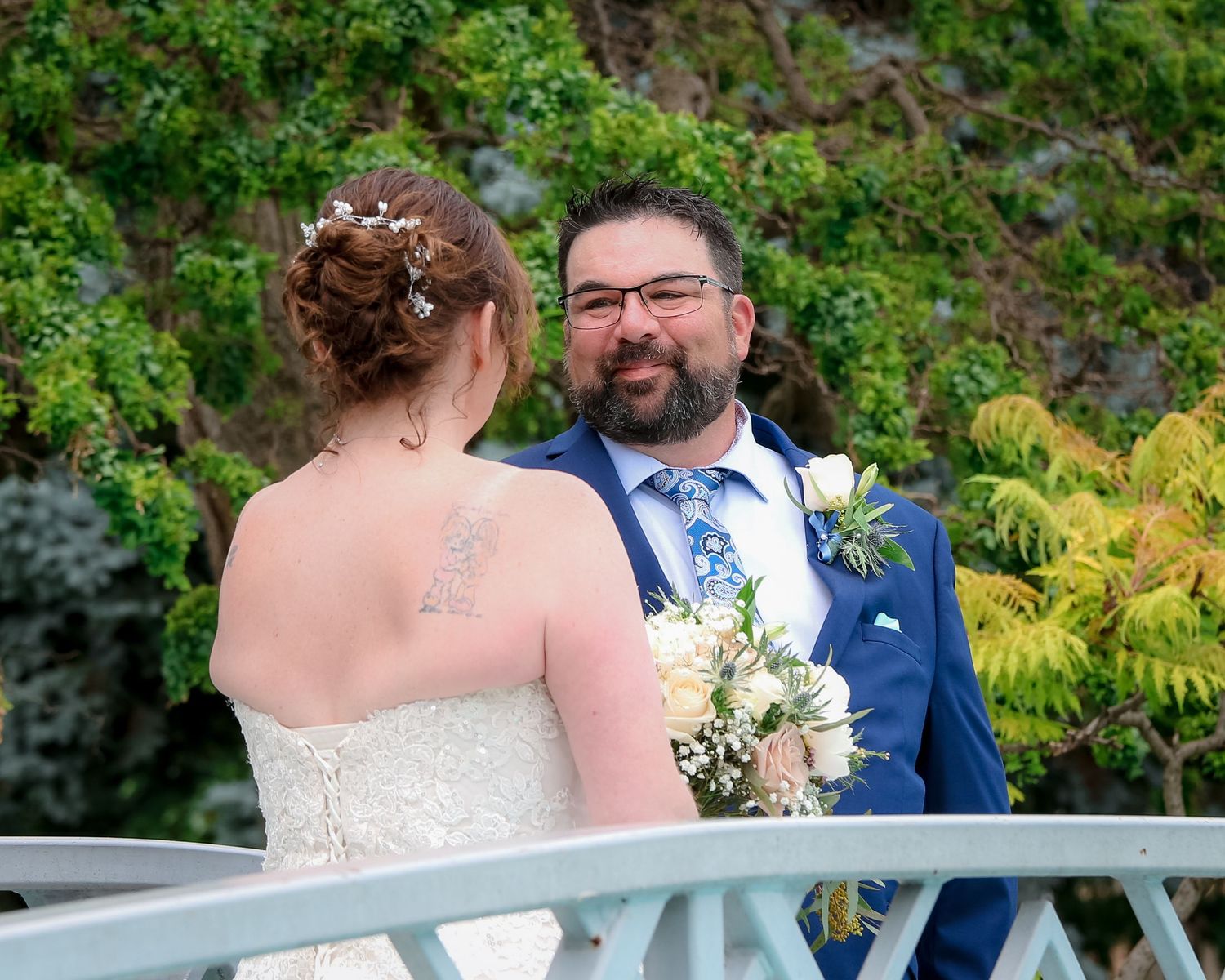 A couple shares a romantic moment during their outdoor wedding ceremony surrounded by lush greenery and ferns.