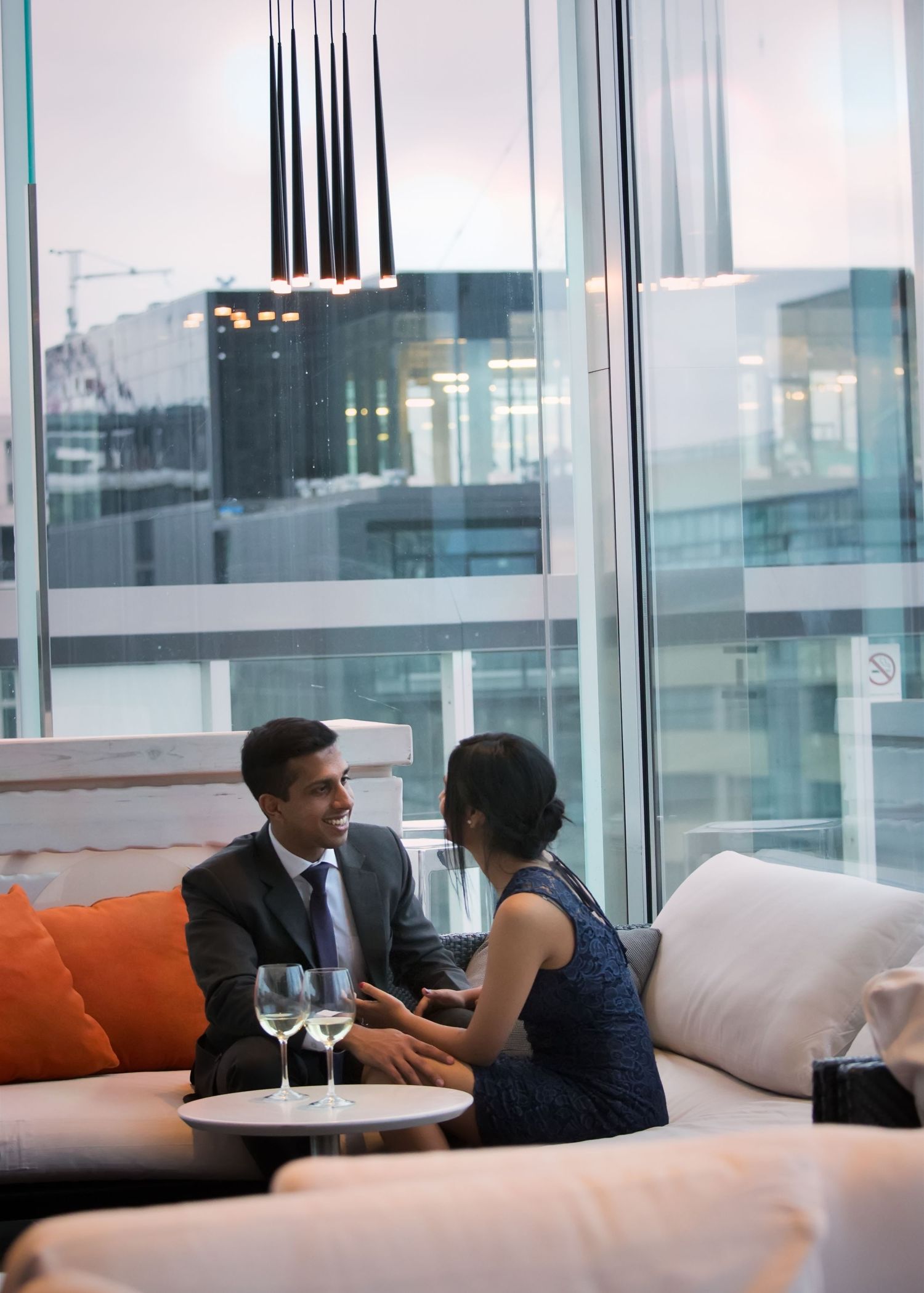 Two business professionals engaged in conversation while sitting on white couches in a modern office lounge area.