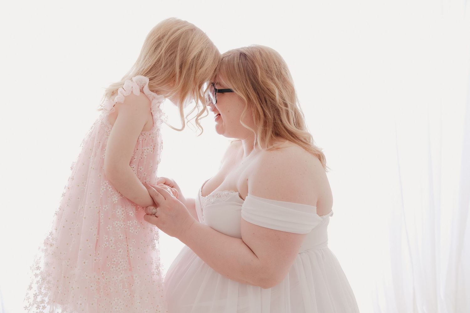 A mother and daughter share a tender moment in matching white and pink dresses.