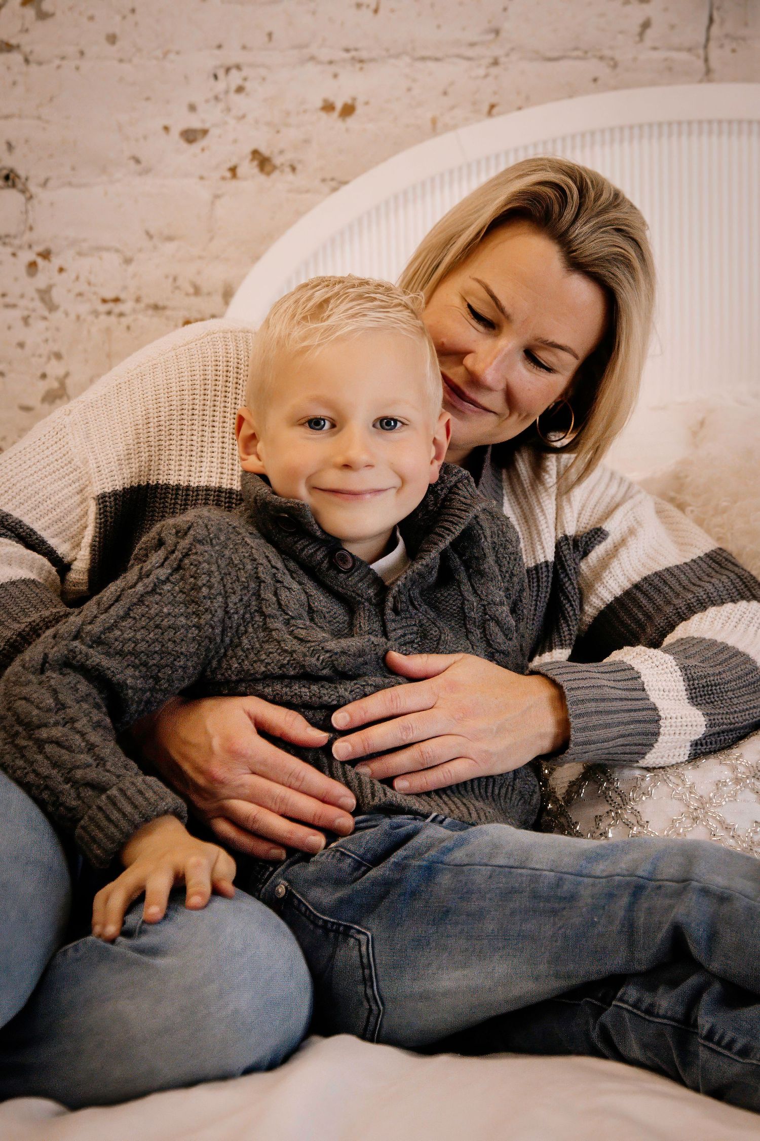 A tender moment captured of parent and child cuddling together on a couch, both wearing cozy knit sweaters.