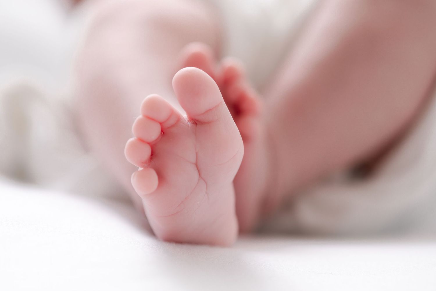 Close up view of tiny newborn baby feet with delicate pink toes against a soft white background.