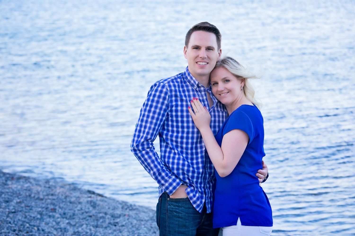 A couple poses for romantic photos at the beach during sunset, wearing blue and plaid outfits.
