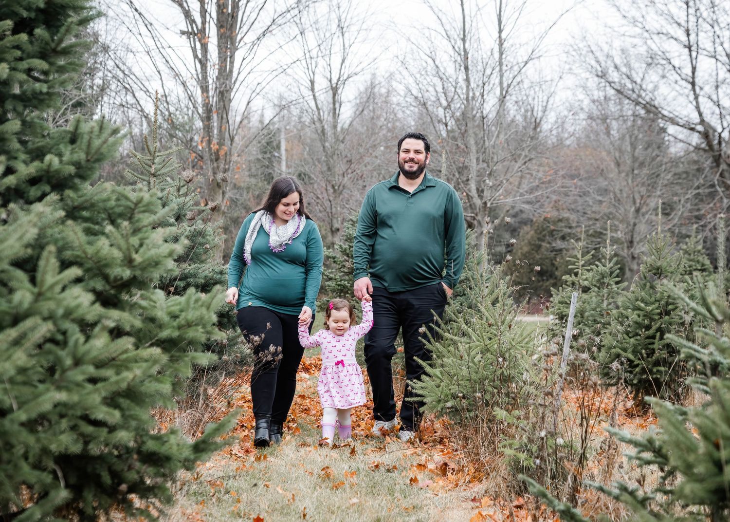 Family walking through rows of evergreen trees at a Christmas tree farm on an autumn day.