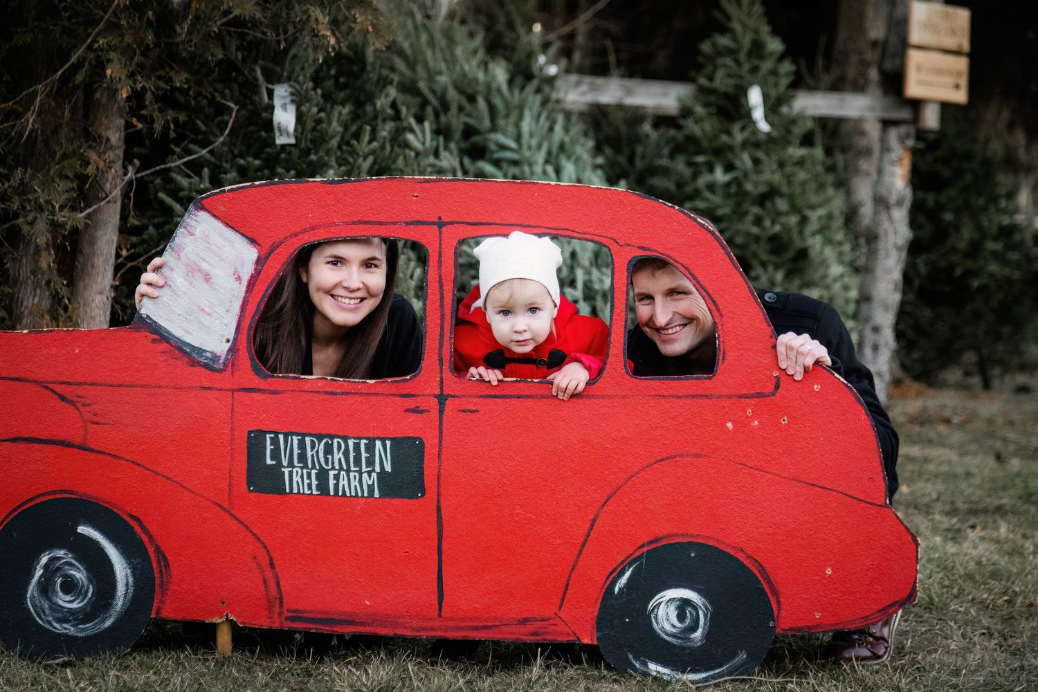 Family members pose together in a vintage bright red classic car outdoors.