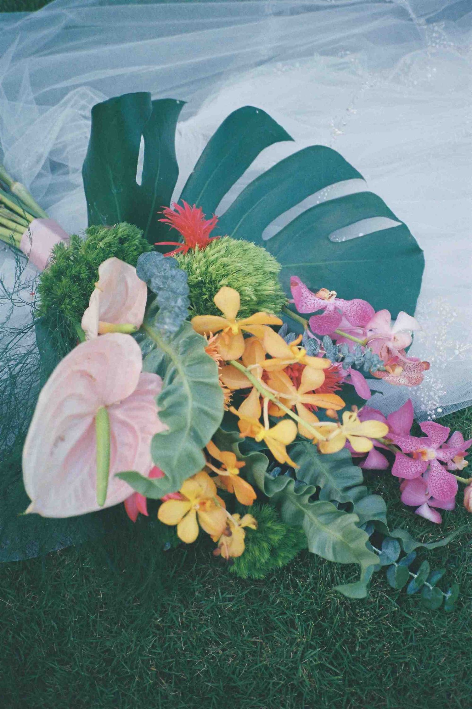 Lang Co wedding: tropical floral arrangement with monstera leaves, orchids and colorful flowers on grass, by AnhVuWedding.