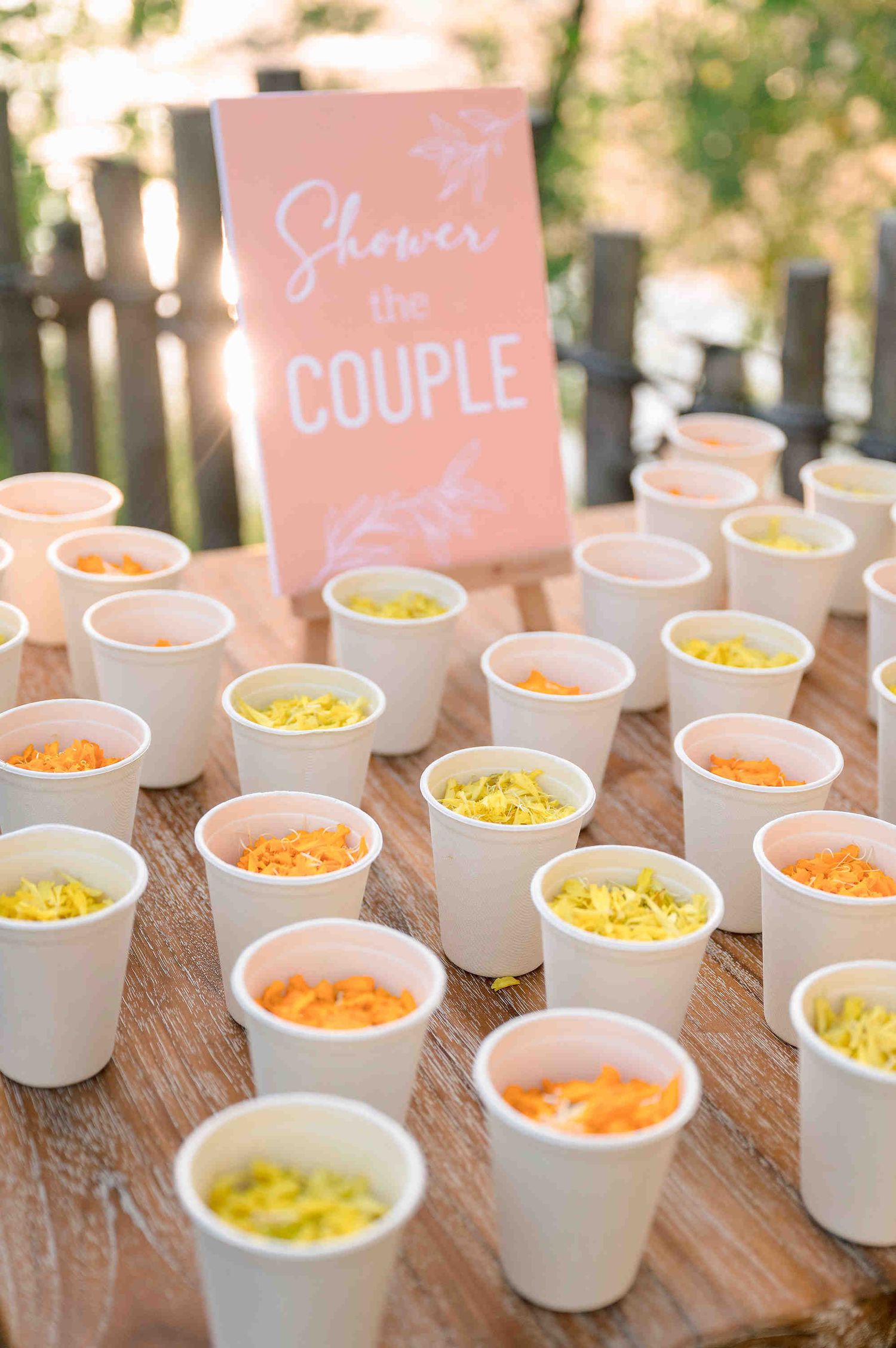 White cups filled with colorful flower petals on a wooden table at a couple shower celebration event.