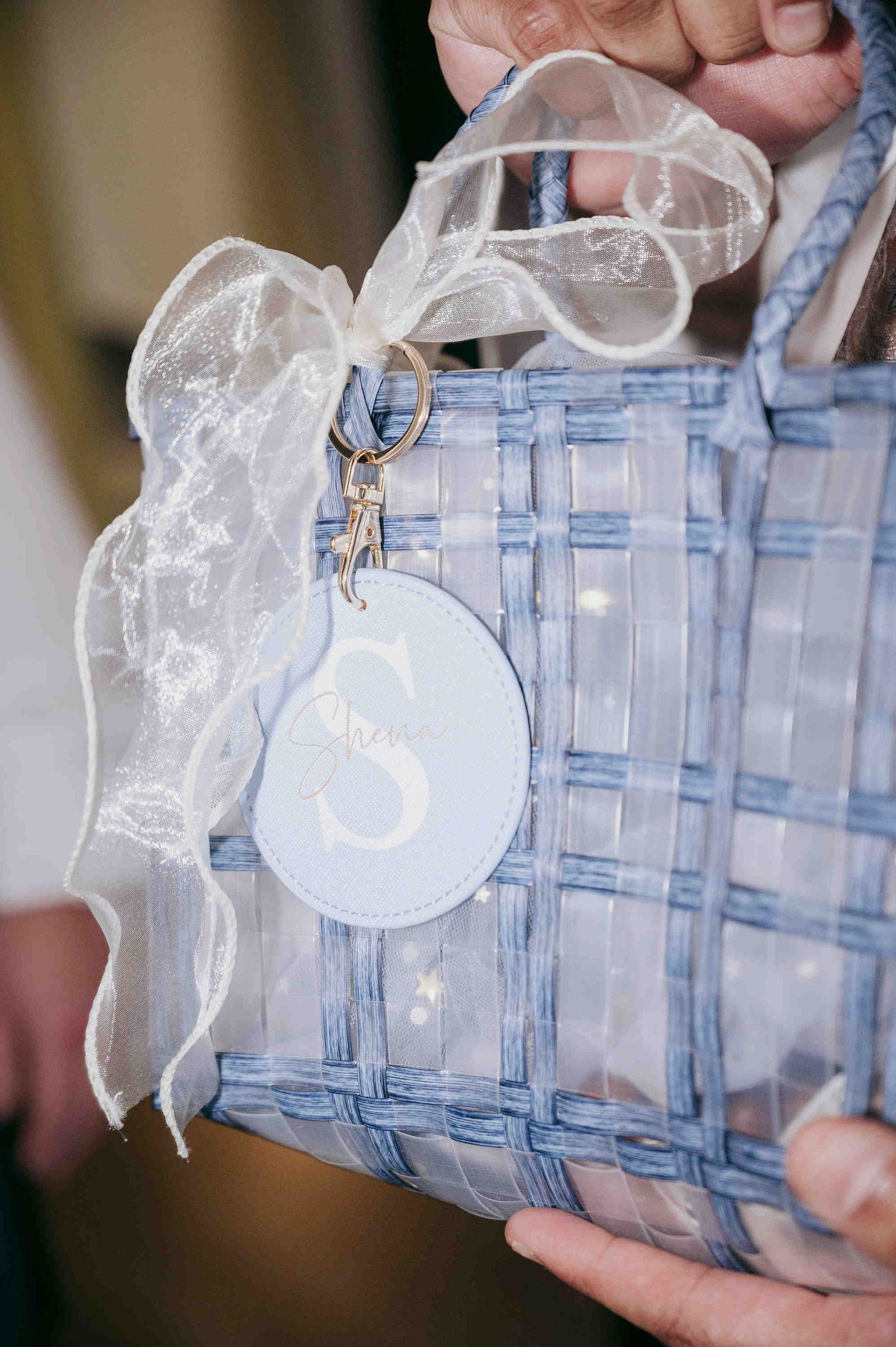 Blue woven transparent tote bag with white organza bow and monogram S leather charm keychain.