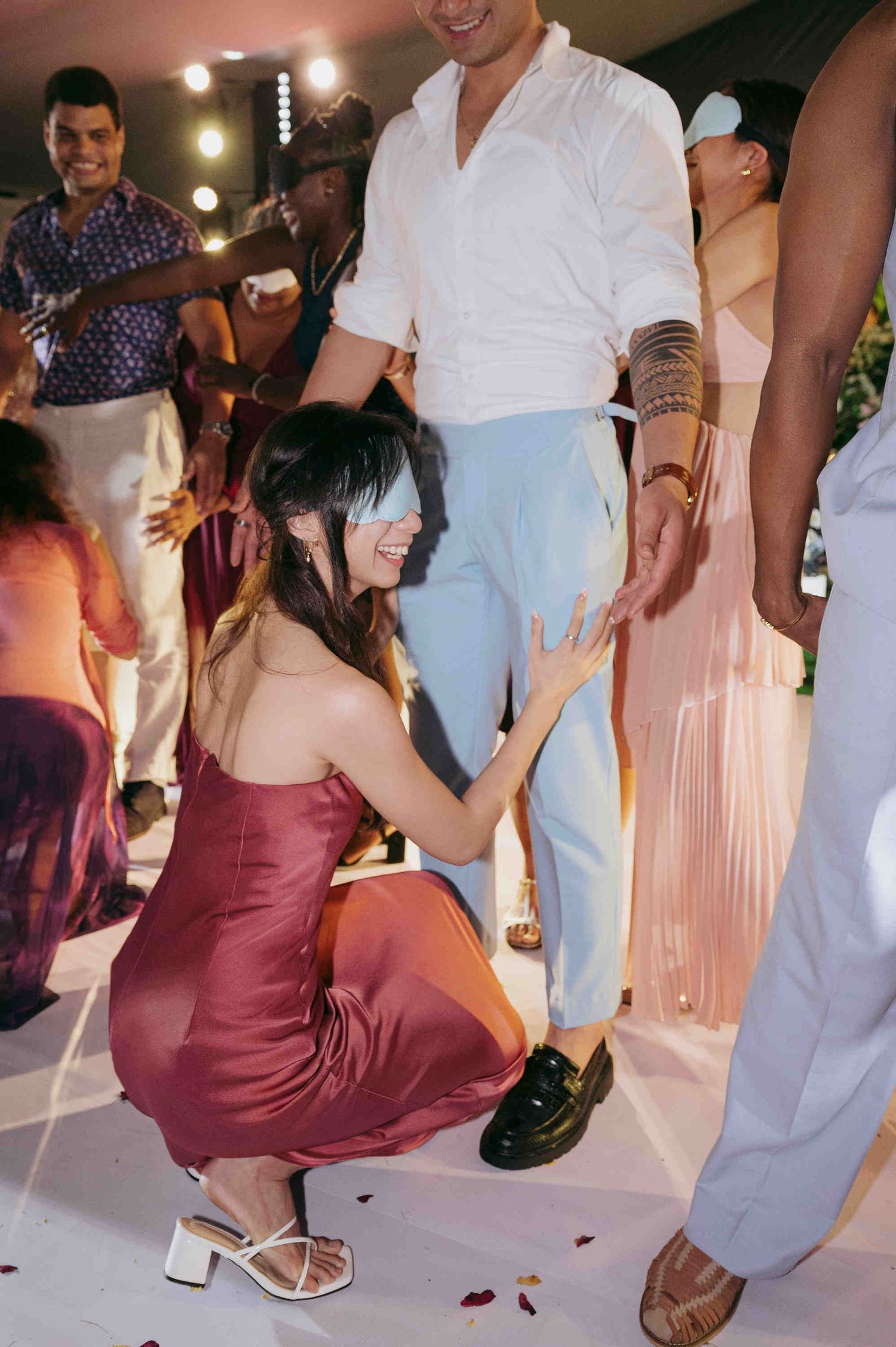 Woman in burgundy satin dress crouching on dance floor at festive wedding reception party.