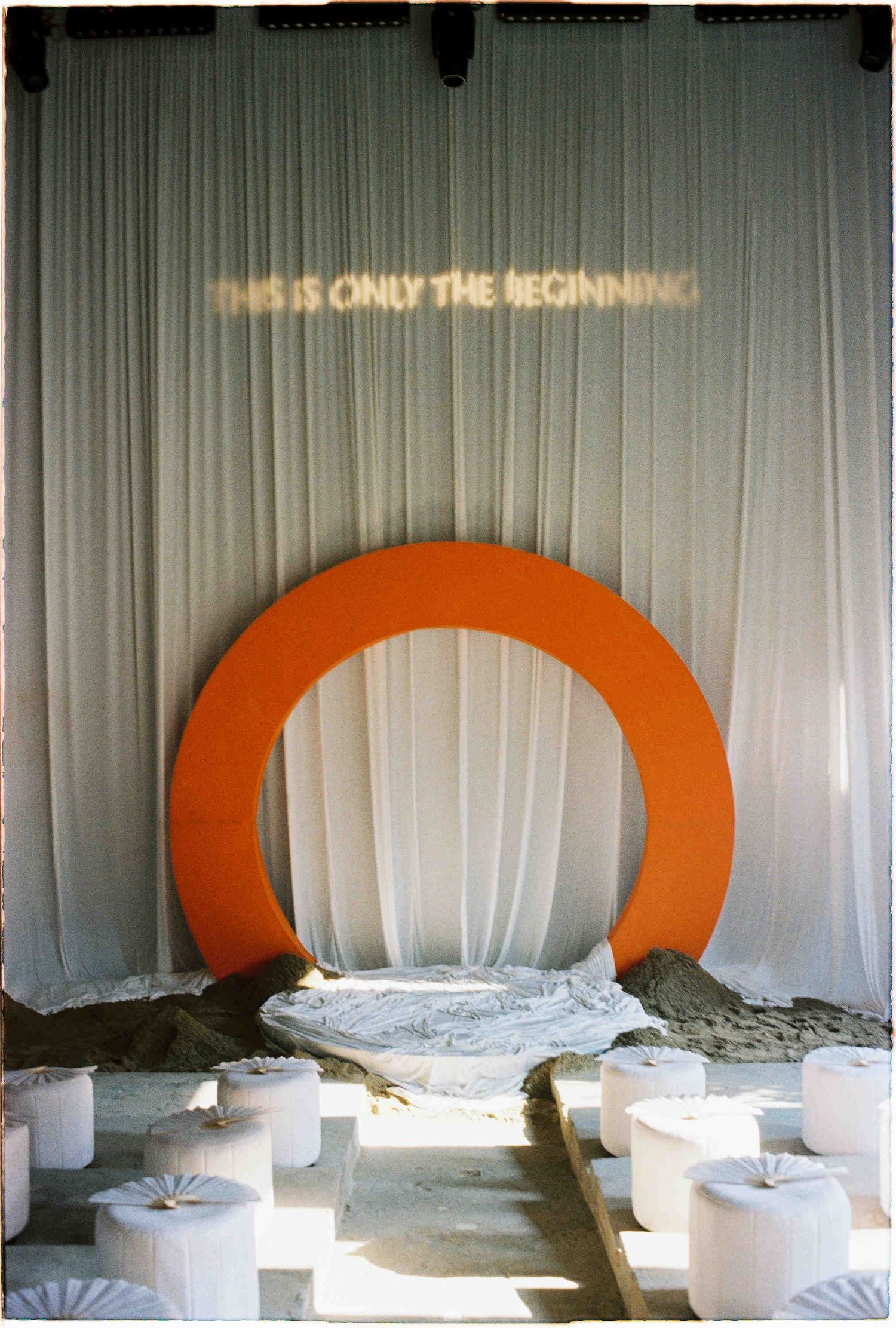 Orange circular arch installation with white draping and neon sign reading THIS IS ONLY THE BEGINNING.