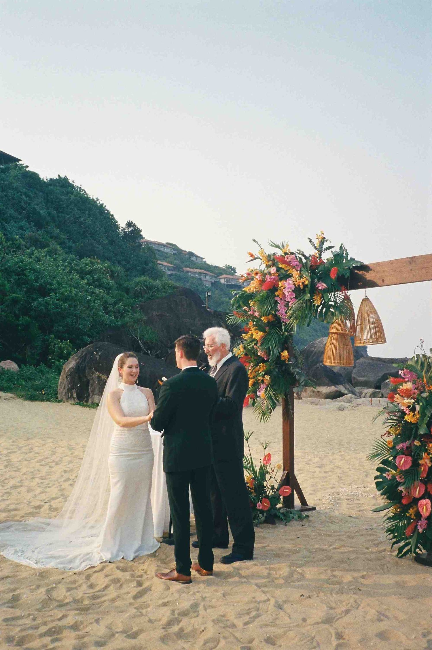 Lang Co wedding ceremony: beach wedding ceremony under floral arch with tropical flowers at sunset, by AnhVuWedding.