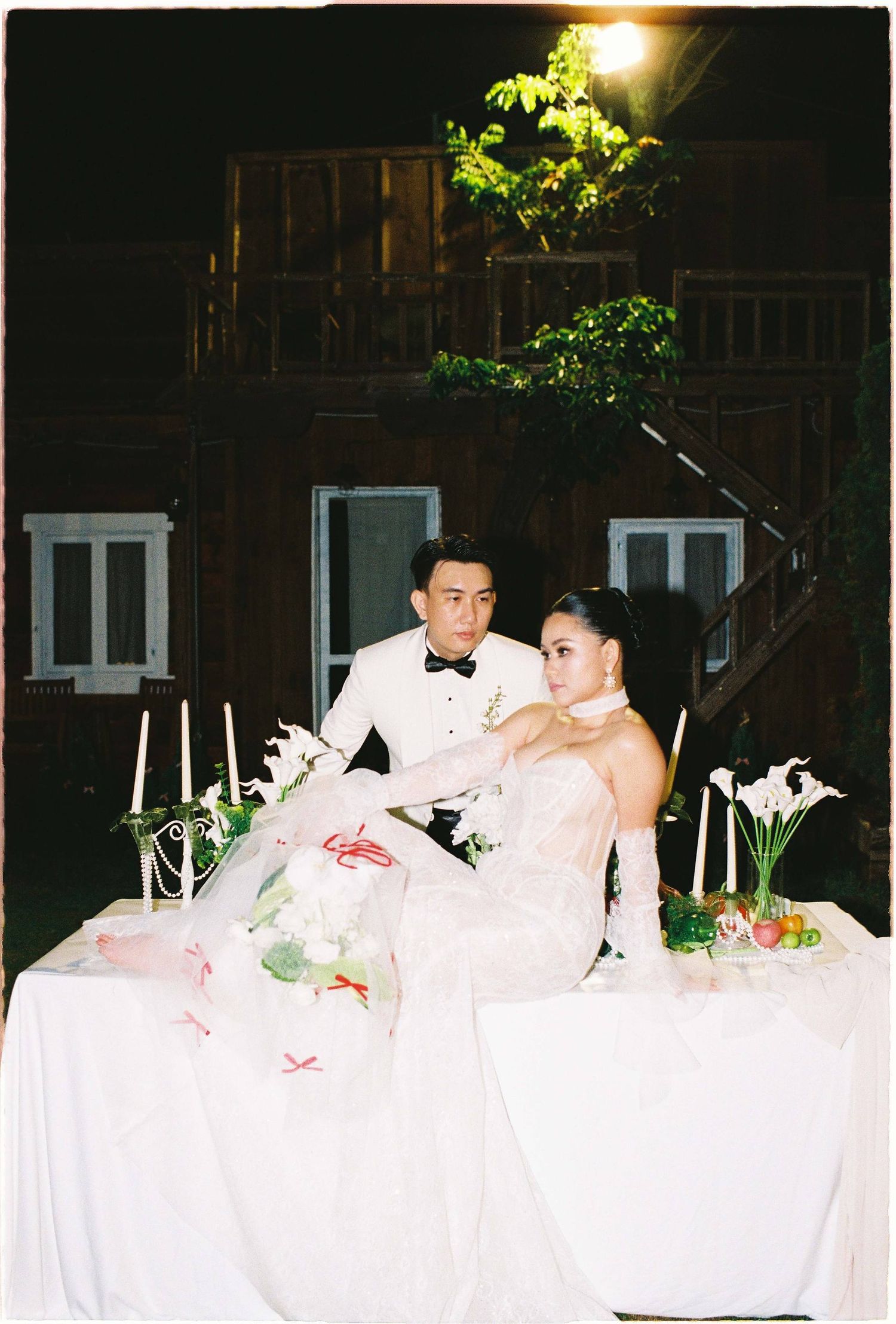 Saigon pre-wedding: newlyweds sit together at an elegantly decorated outdoor table with white floral arrangements, by AnhVuWedding.