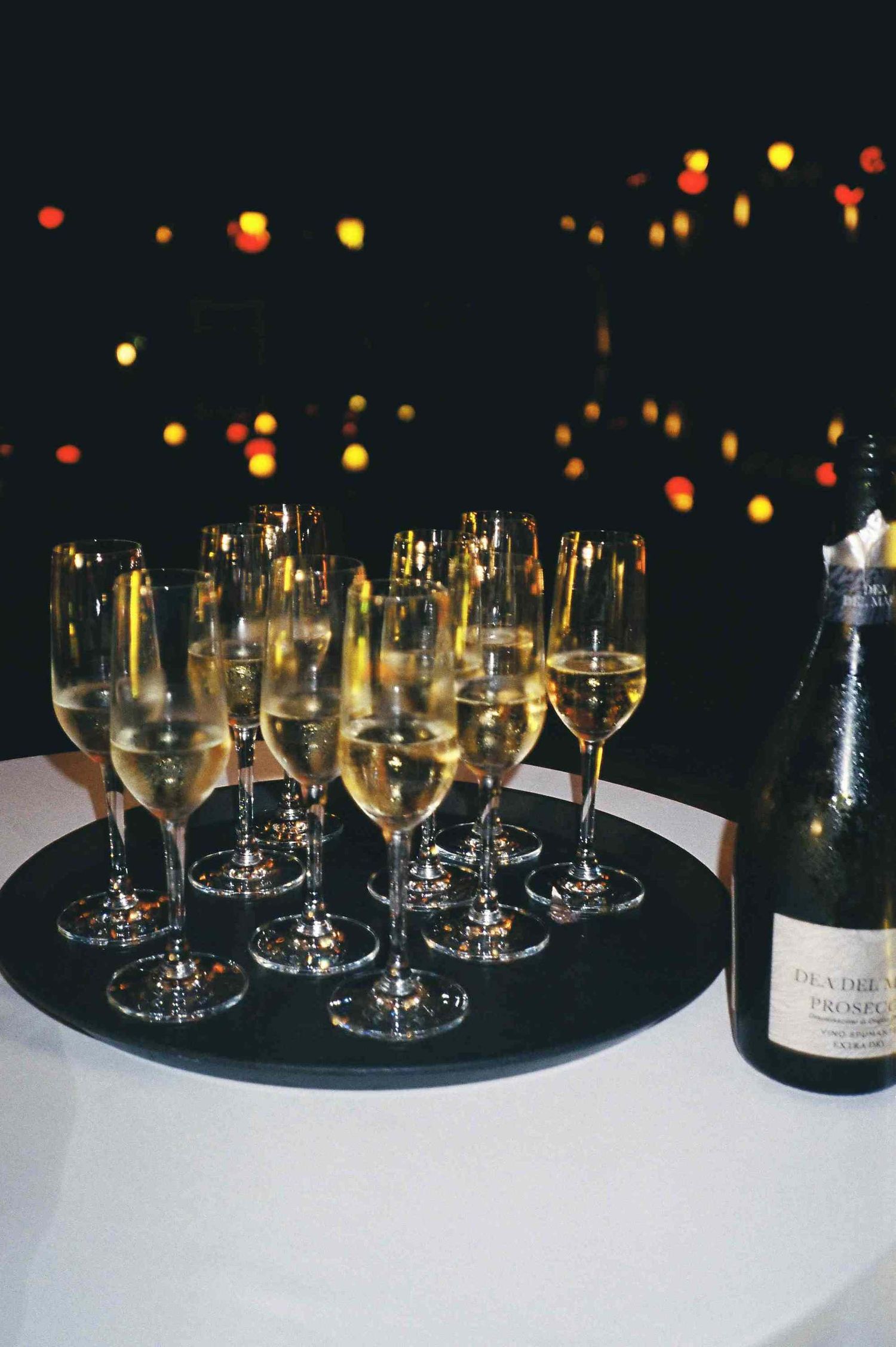 Lang Co wedding: row of champagne glasses and wine bottles arranged on dark table with twinkle lights in background, by AnhVuWedding.