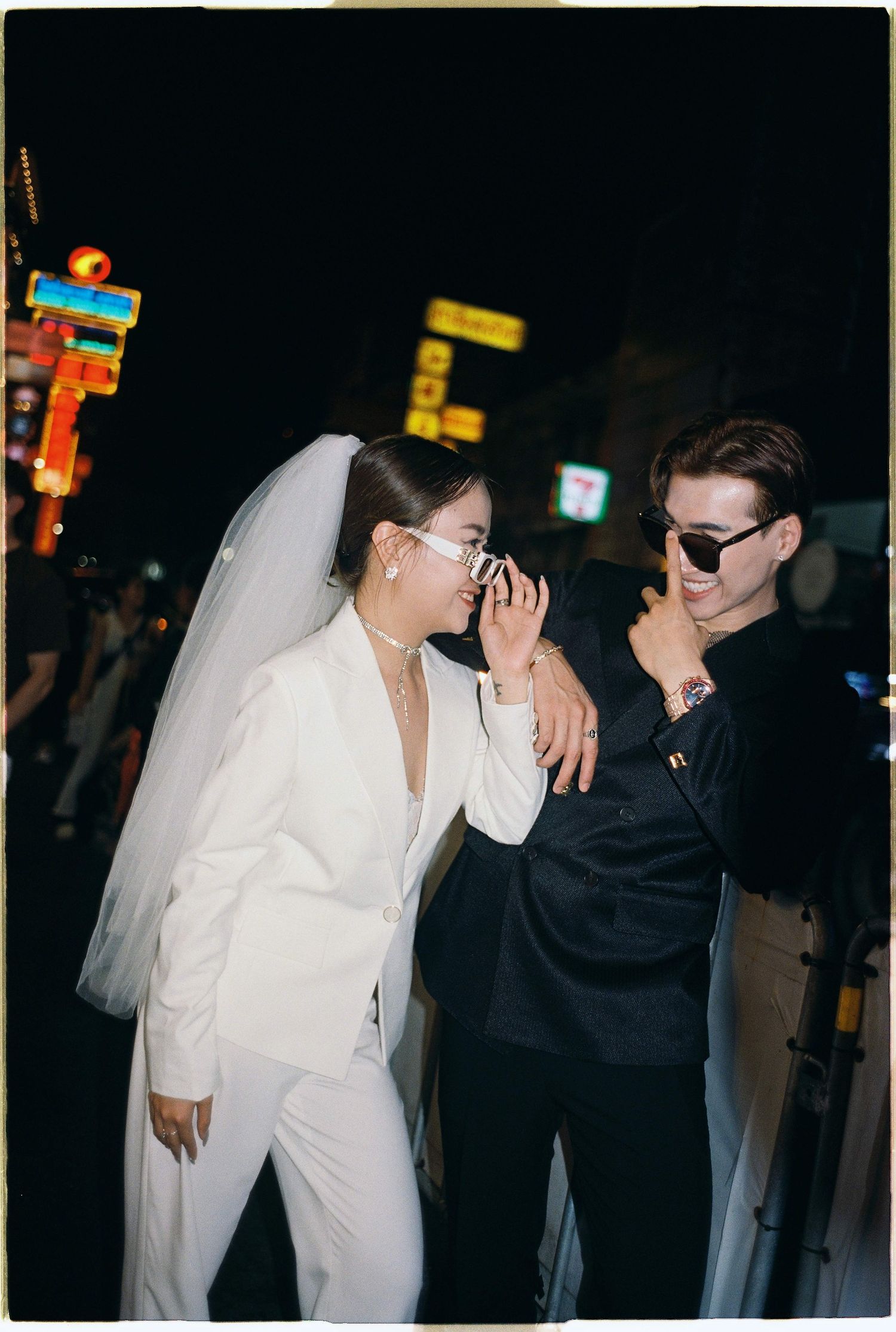 Saigon pre-wedding: two figures in black and white attire lean against each other on a dark city street, by AnhVuWedding.