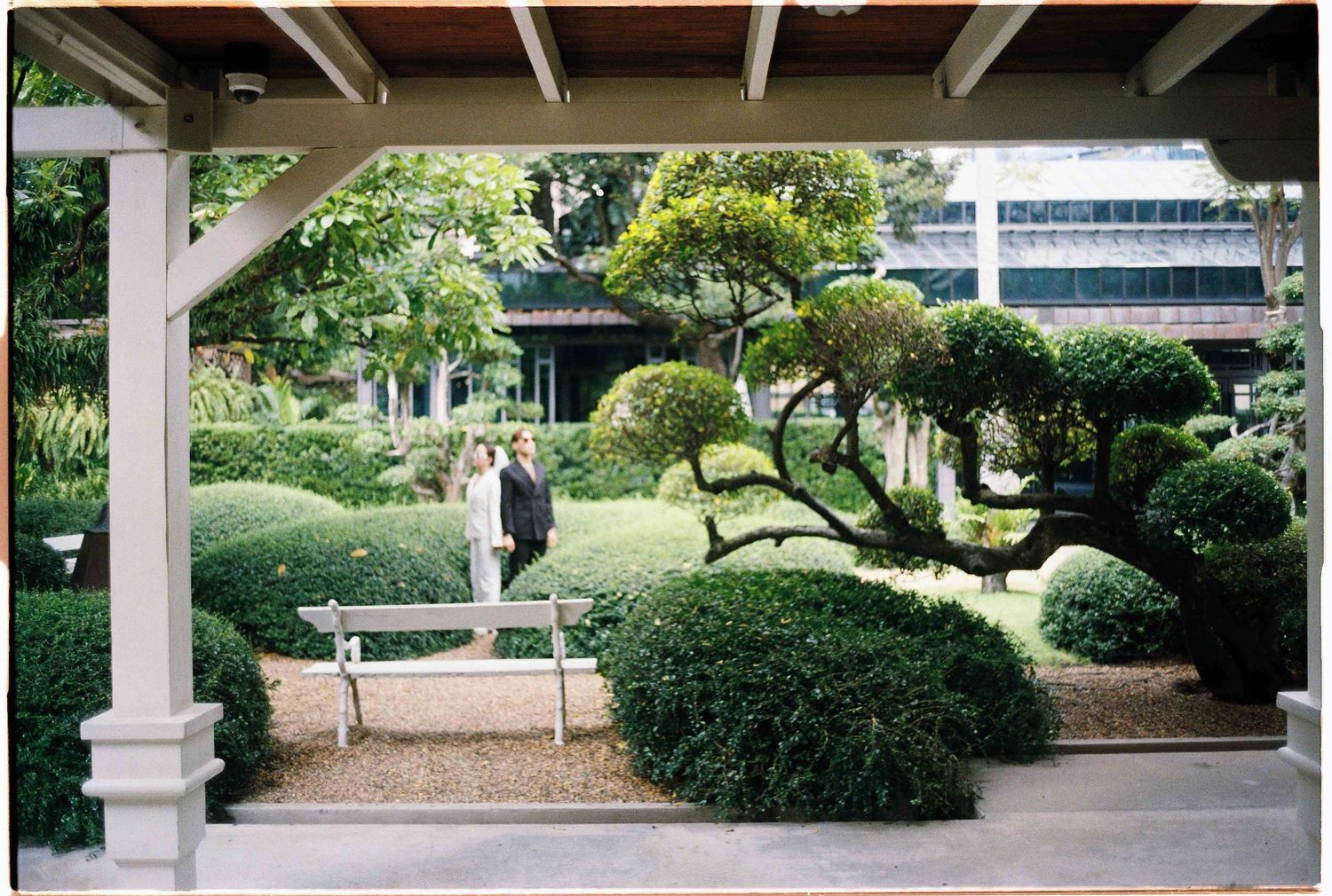 Saigon pre-wedding: covered outdoor walkway with white columns and lush greenery in a garden setting, by AnhVuWedding.