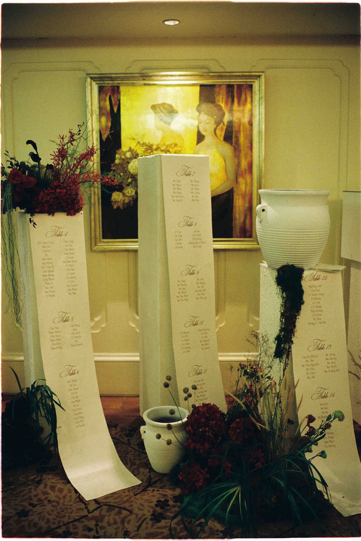 Elegant wedding seating chart display with tall white columns, floral arrangements, and a classic portrait painting backdrop.
