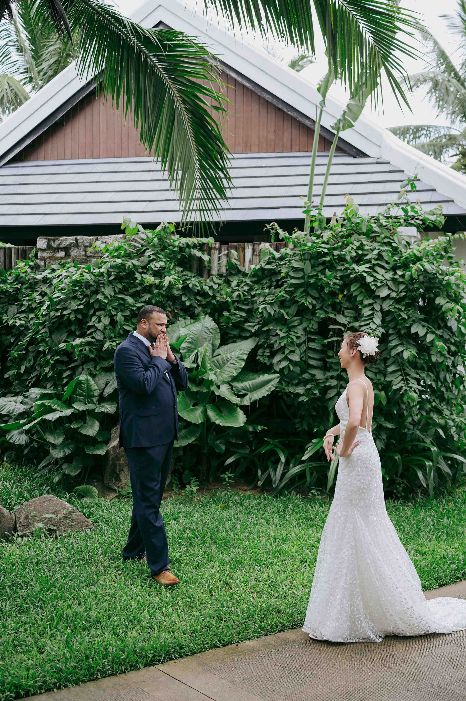 Groom emotional at first look with bride in white gown, tropical garden wedding venue with lush greenery.