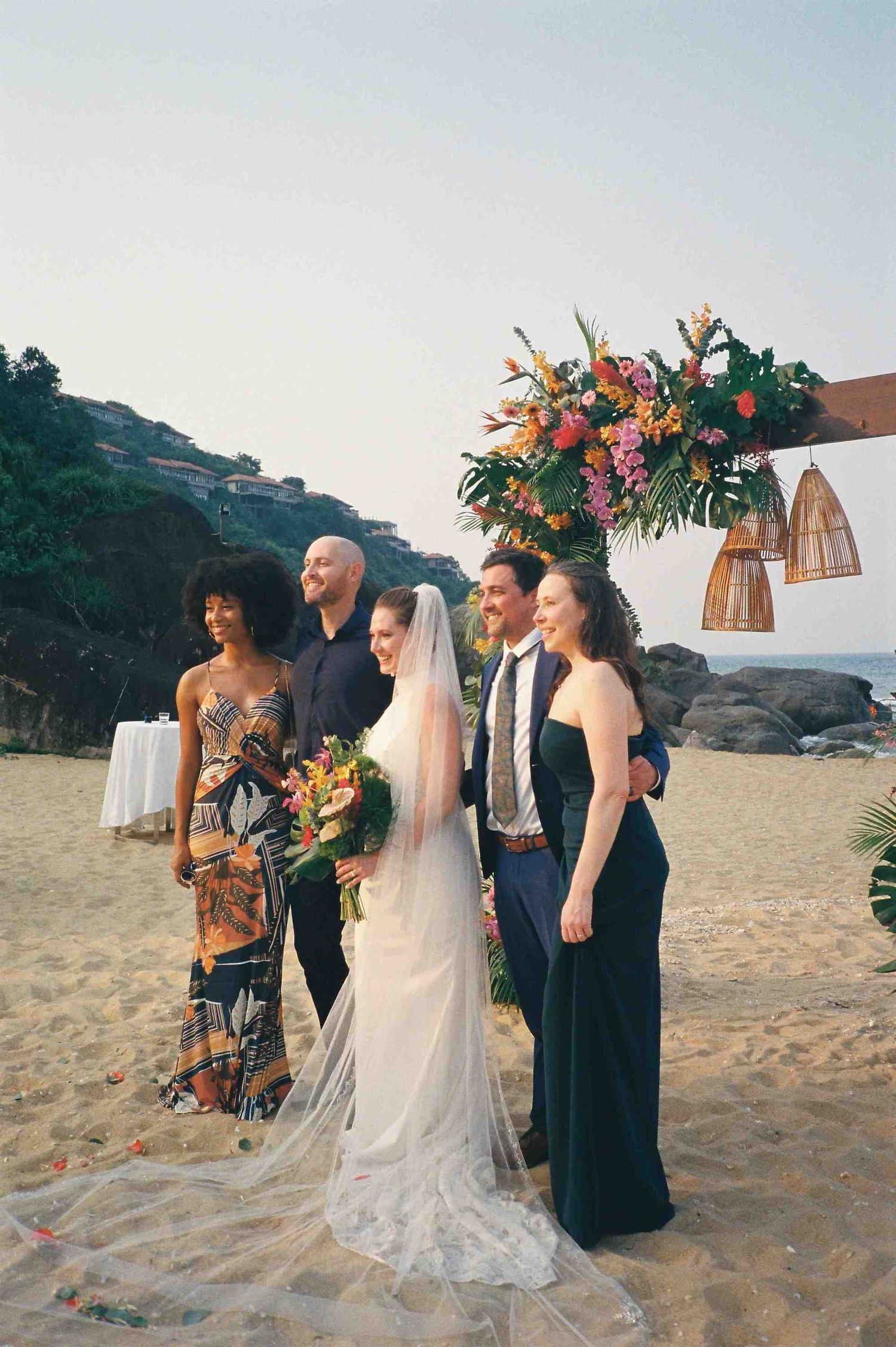 Lang Co wedding: wedding party poses for photos on sandy beach with floral arch and ocean view, by AnhVuWedding.
