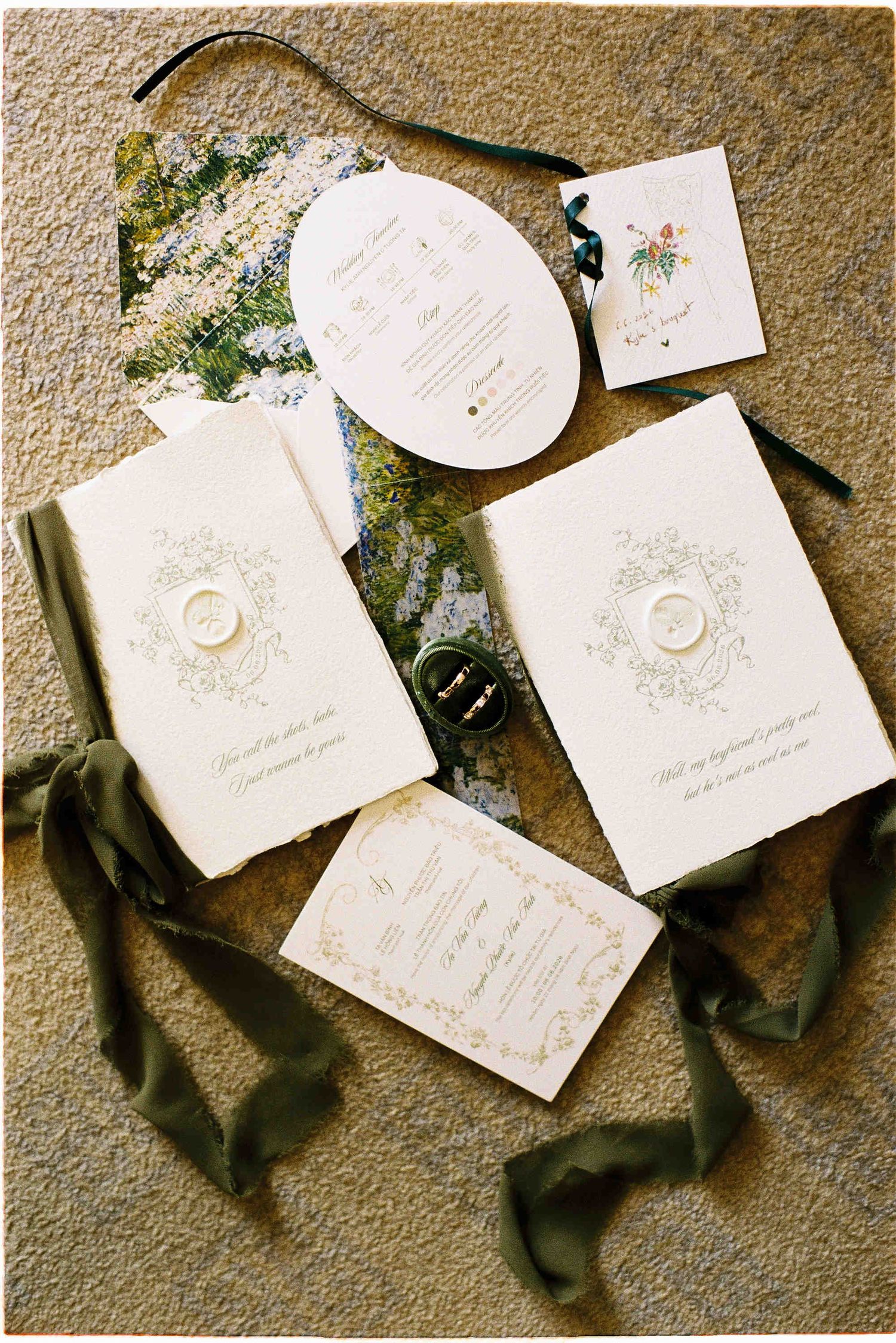 Elegant wedding stationery suite with ivory booklets, olive green ribbons, wax seals, and floral accents on a textured surface.