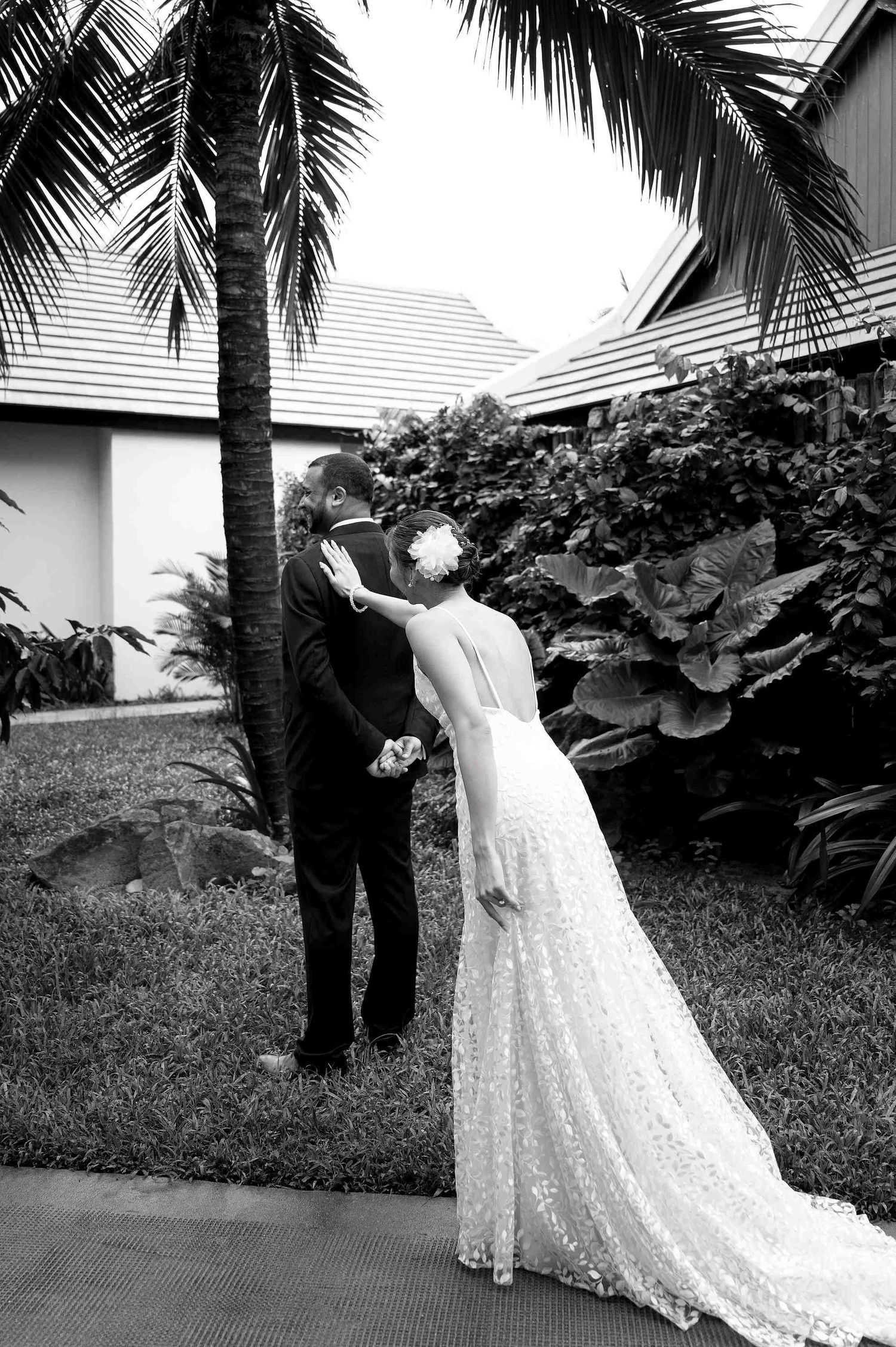 Bride and groom share a romantic kiss under a palm tree in a tropical garden in black and white.