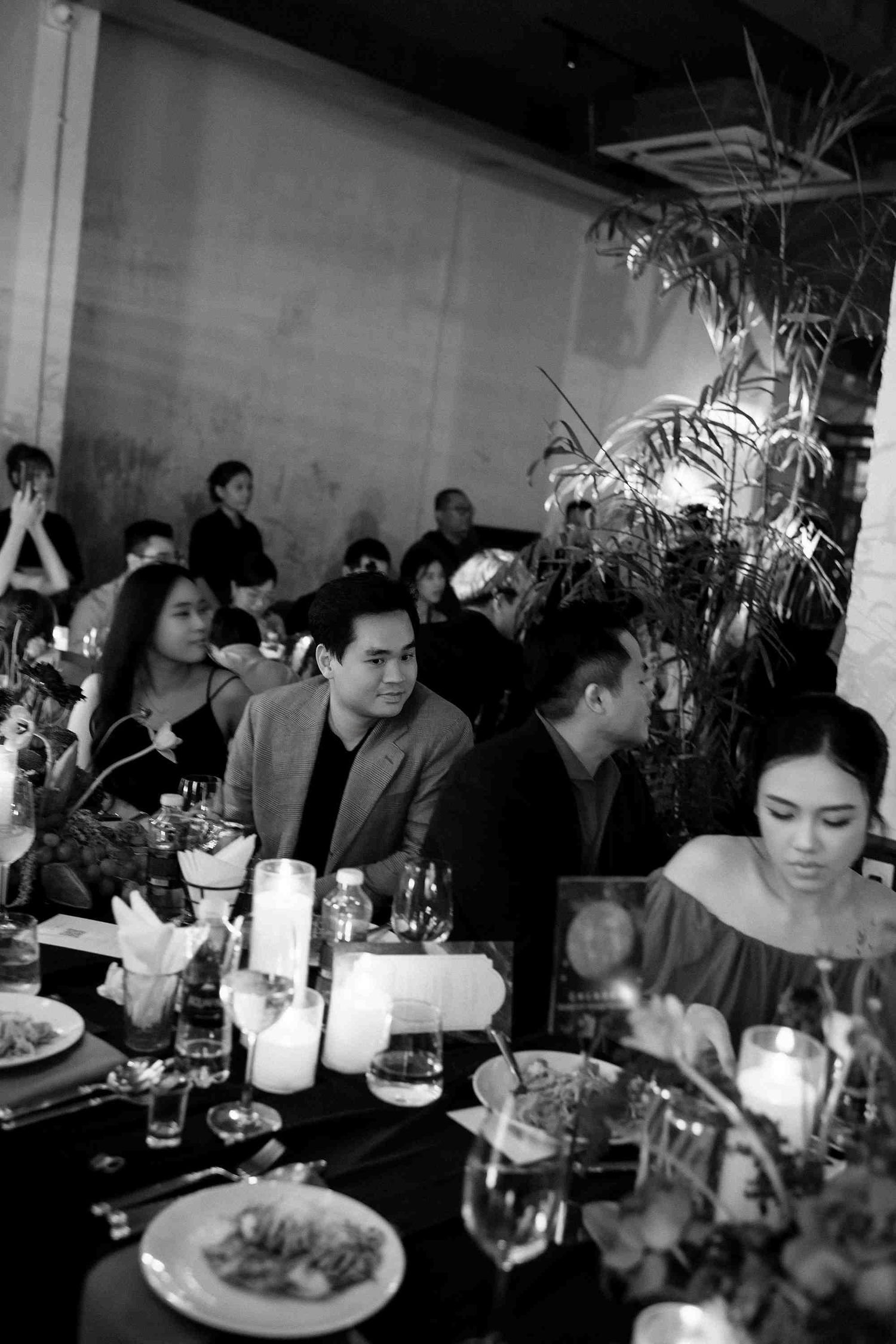 Black and white photo of elegantly dressed guests seated at a candlelit dinner table at a formal event.