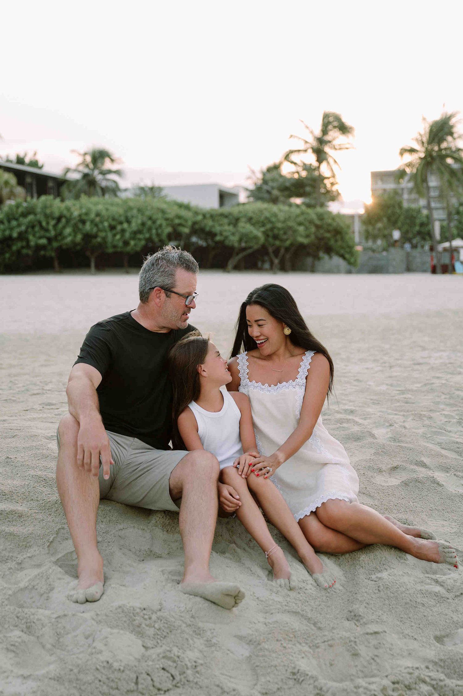 Da Nang family: couple sits together on a sandy beach during sunset, sharing intimate moments, by AnhVuWedding.
