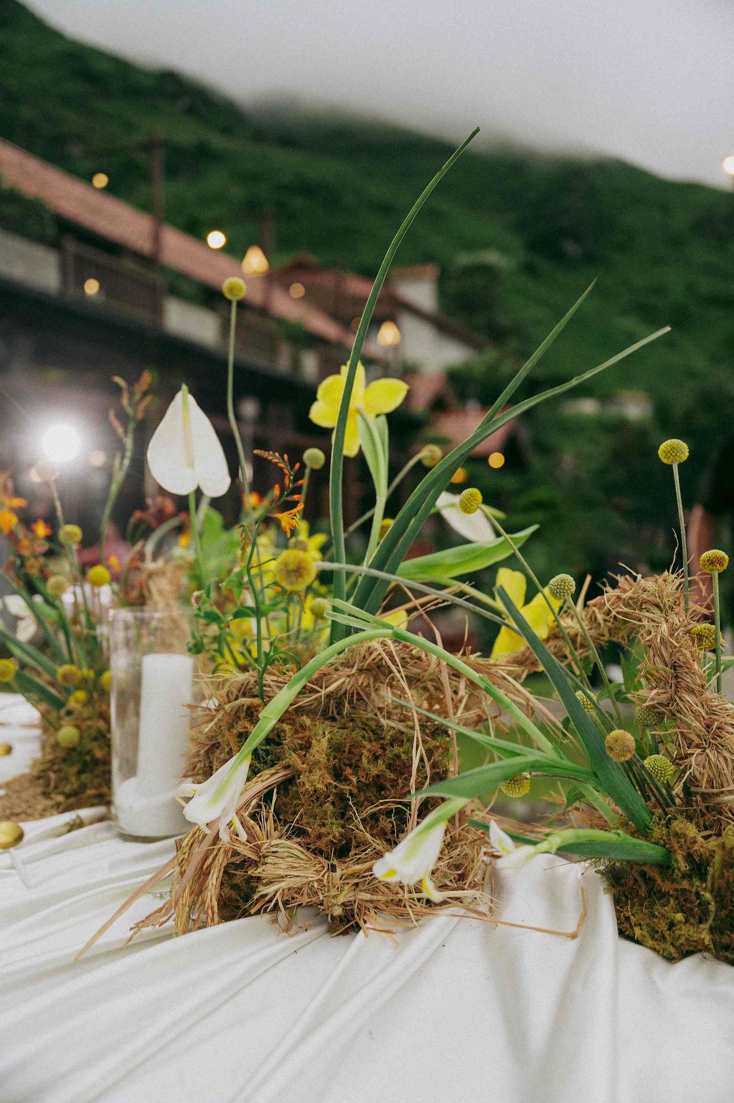 wedding: wedding table centerpiece featuring hay, yellow flowers and white candles in glass holders, by AnhVuWedding.