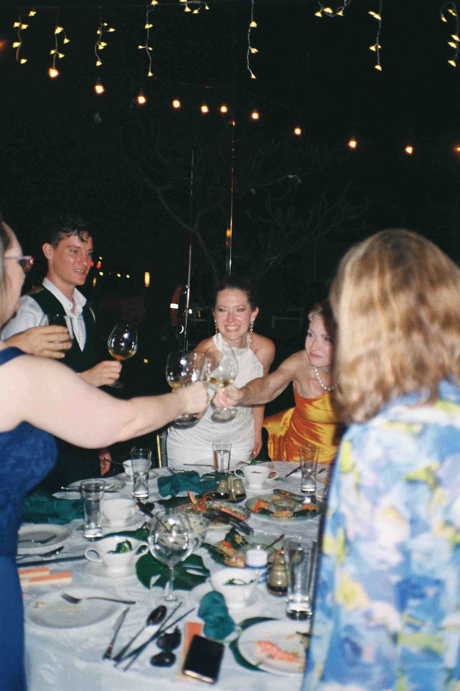 Lang Co wedding reception: wedding guests enjoying dinner and conversation under string lights at outdoor reception, by AnhVuWedding.