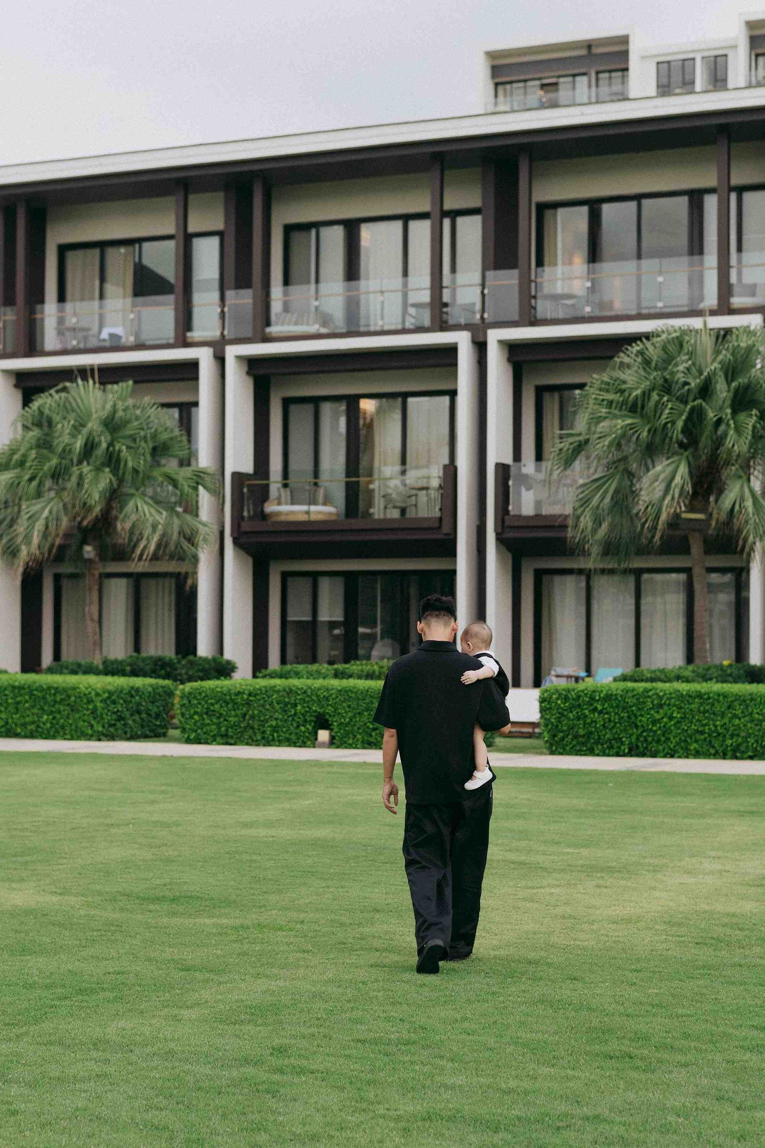 Da Nang family: figures walking across a manicured lawn in front of a modern building, by AnhVuWedding.