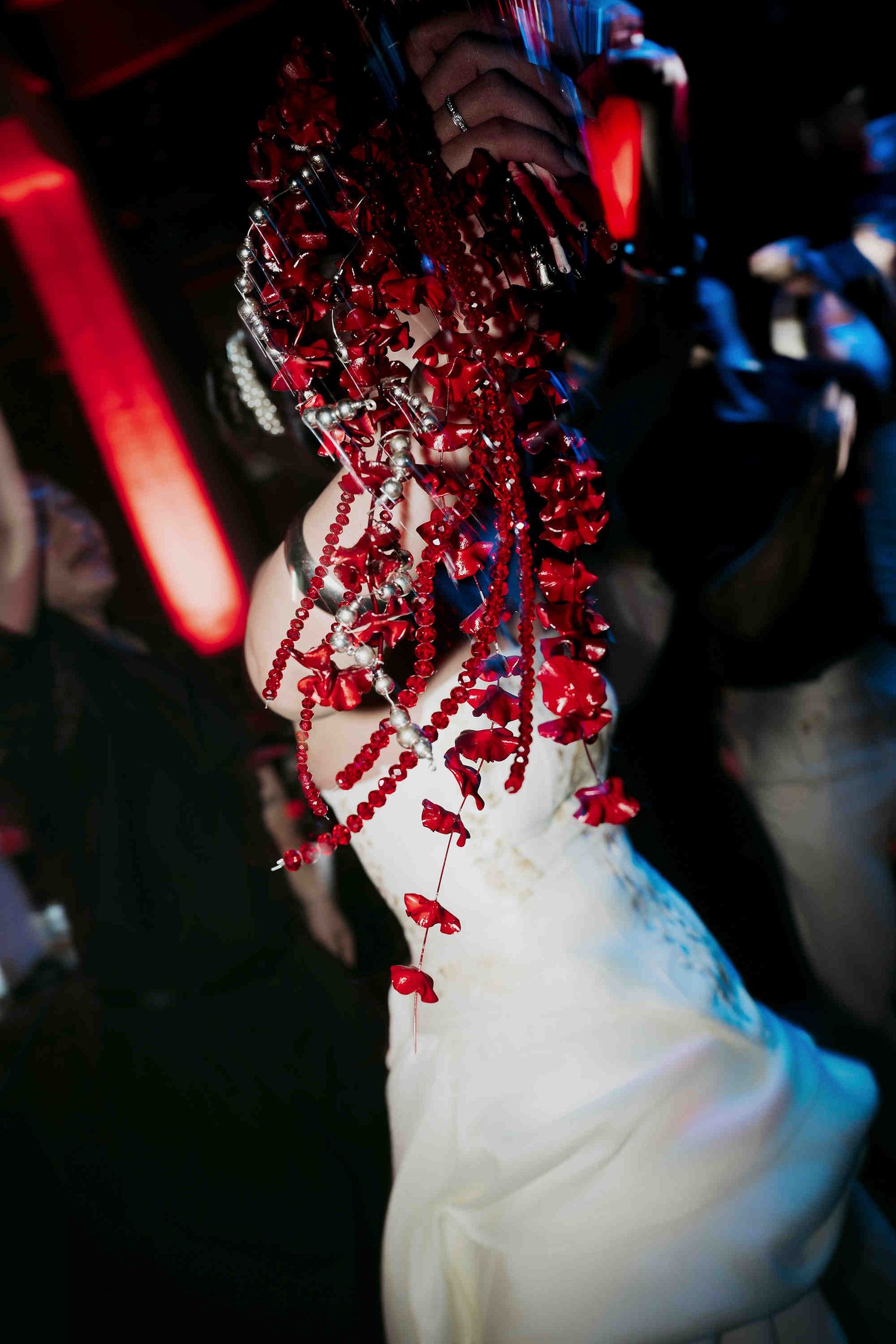 Bride in white gown adorned with cascading red floral beaded headpiece at a dark, atmospheric wedding reception.