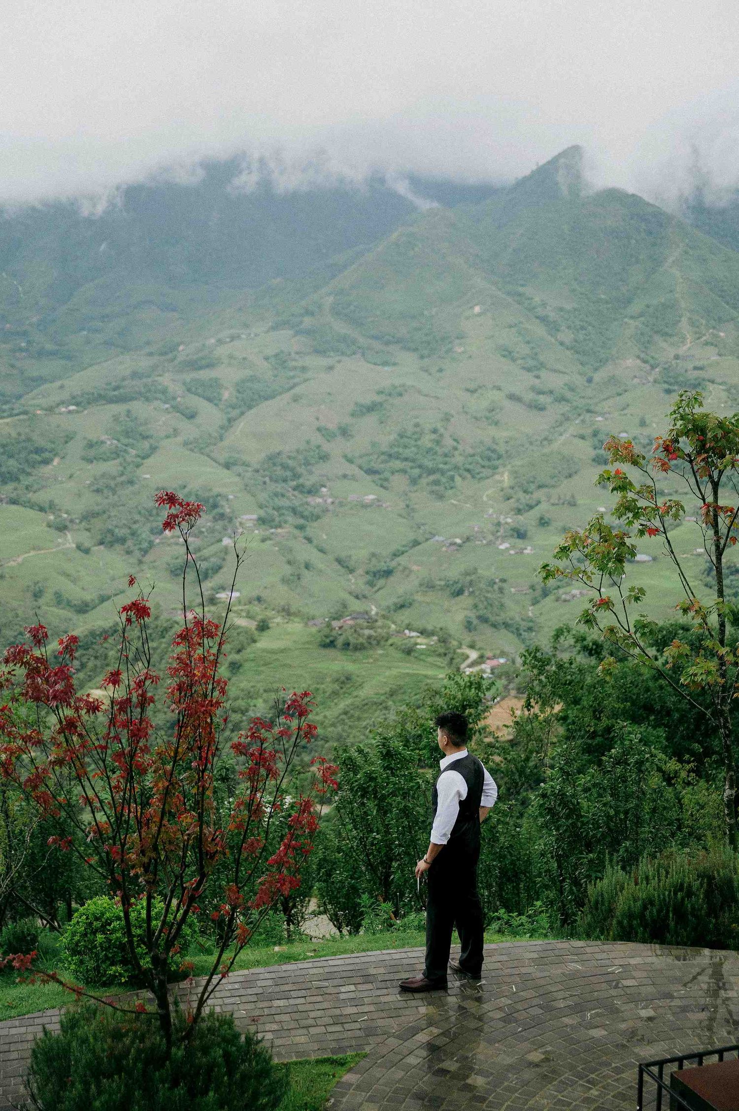 wedding: scenic mountain landscape with red flowering trees and a viewing platform overlooking green hills and misty peaks, by AnhVuWedding.