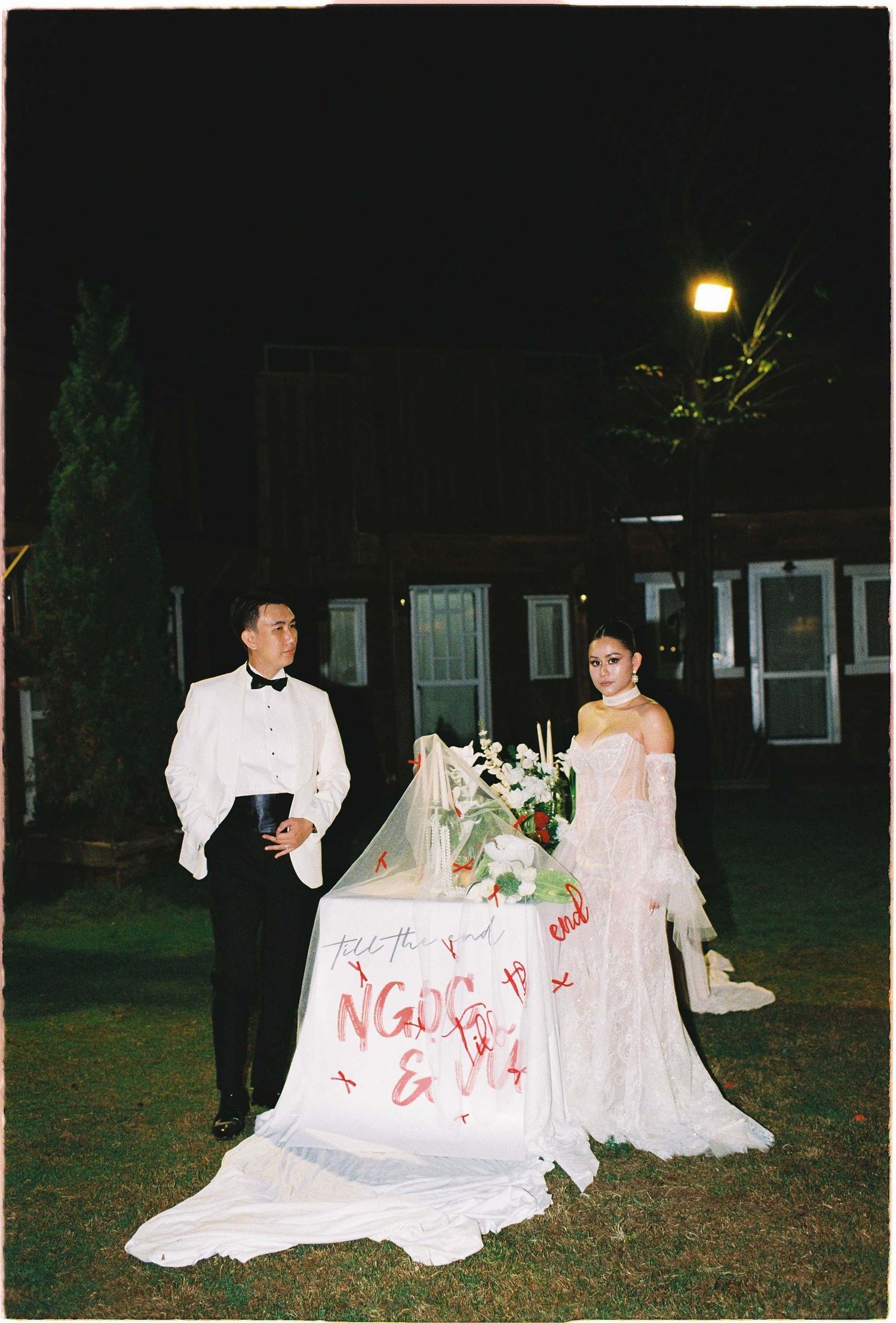 Saigon pre-wedding: formal wedding photo of a couple standing beside an elegantly decorated white table at night, by AnhVuWedding.