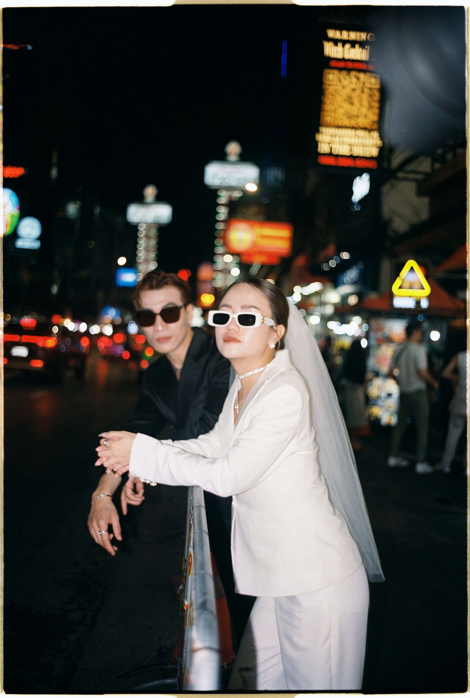Saigon pre-wedding: people in sunglasses and contrasting outfits pose dramatically on a city street at night, by AnhVuWedding.