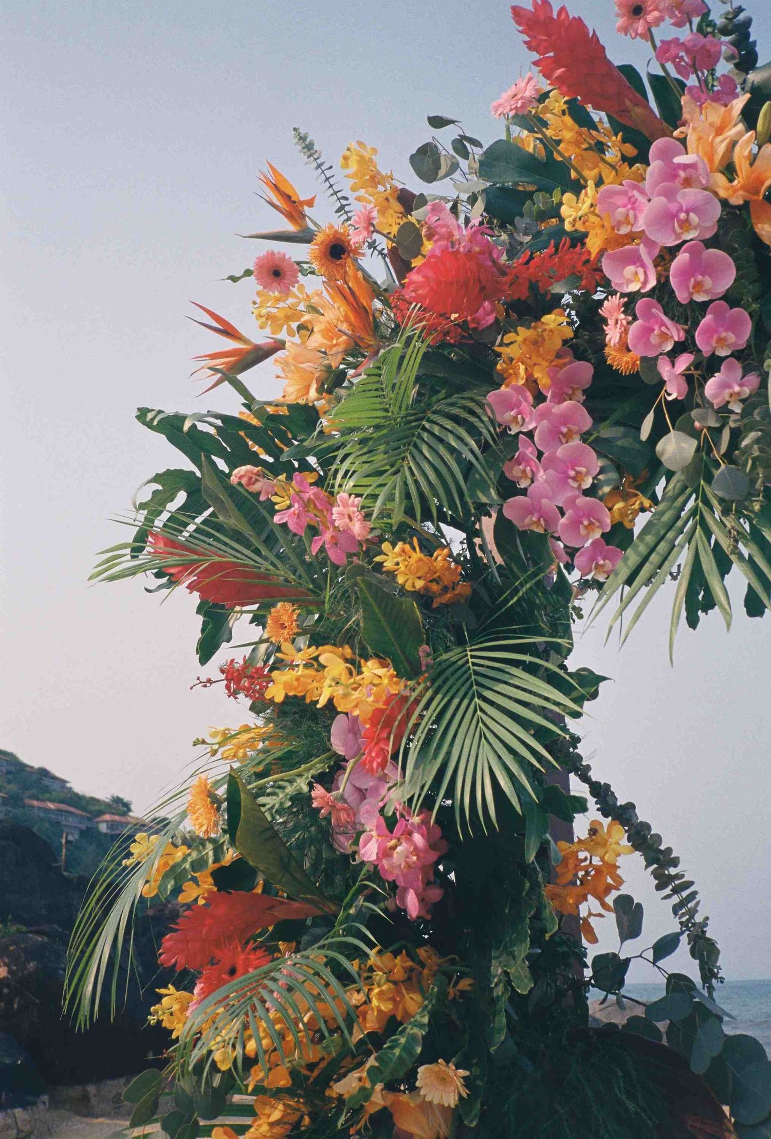 Lang Co wedding: stunning tropical flower arrangement with orchids, birds of paradise, and palm fronds against sky, by AnhVuWedding.