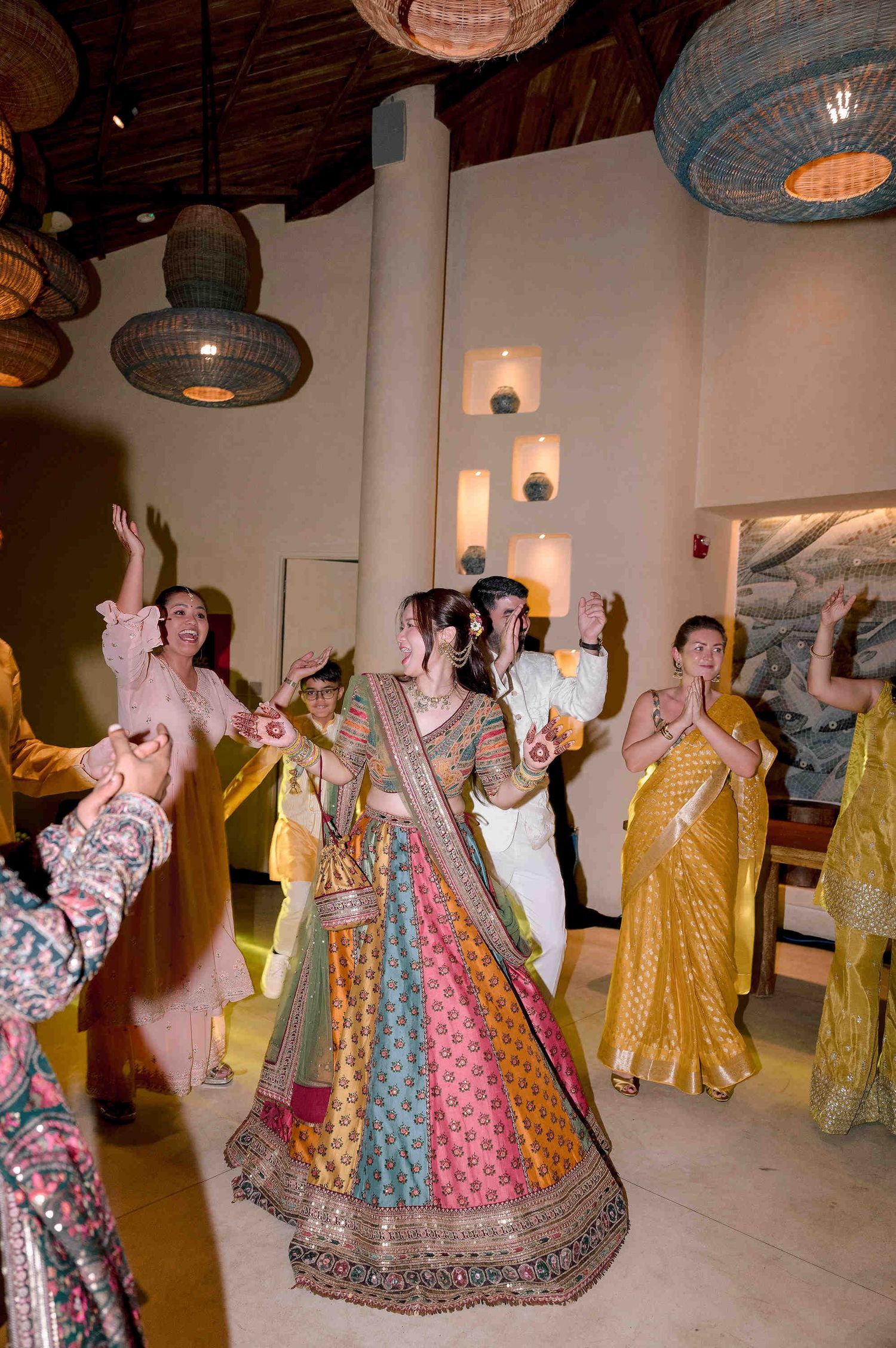 Bride in colorful lehenga dancing with guests in traditional Indian attire at a vibrant wedding celebration.