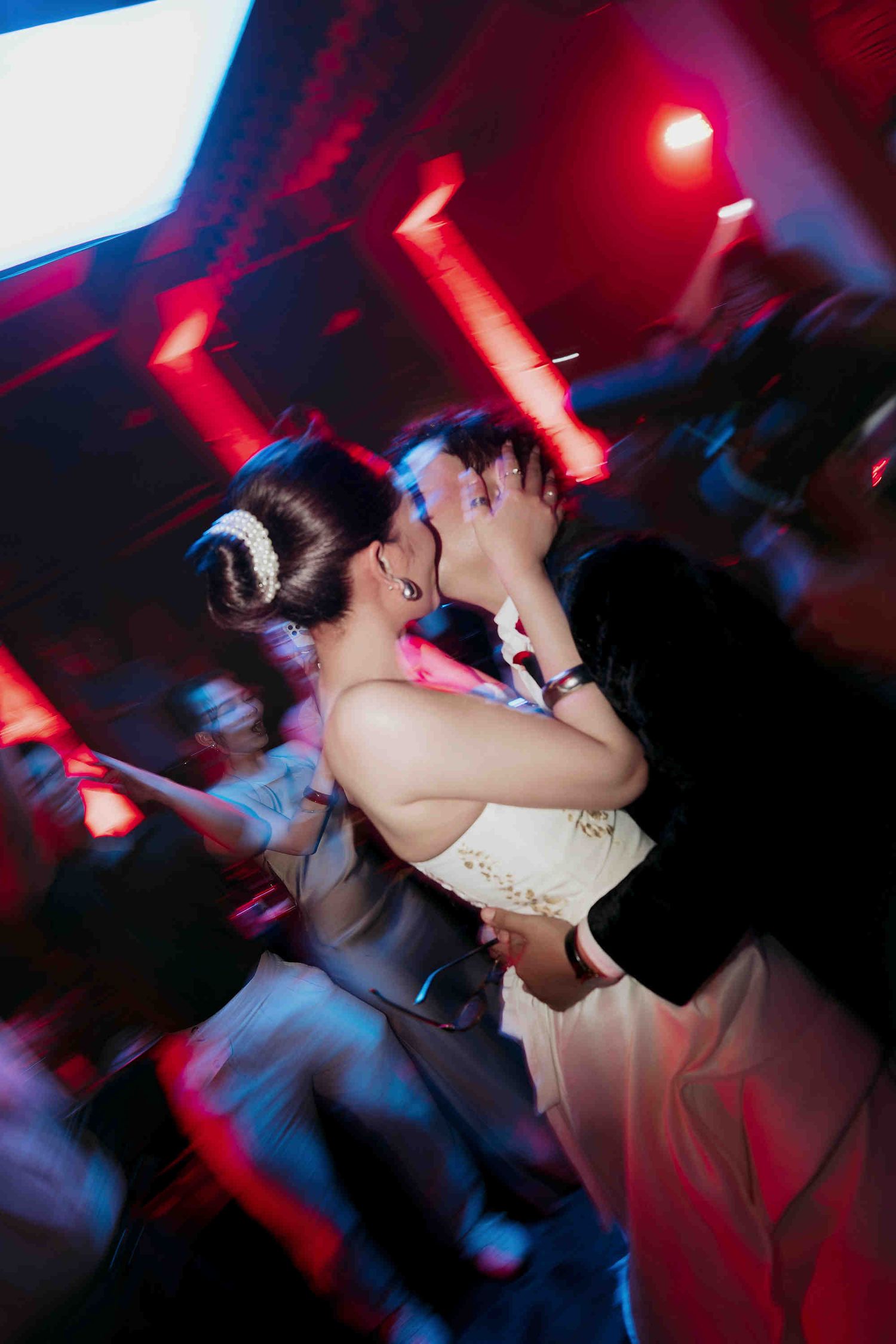 Bride and groom share a romantic first dance kiss under red lights at their wedding reception.