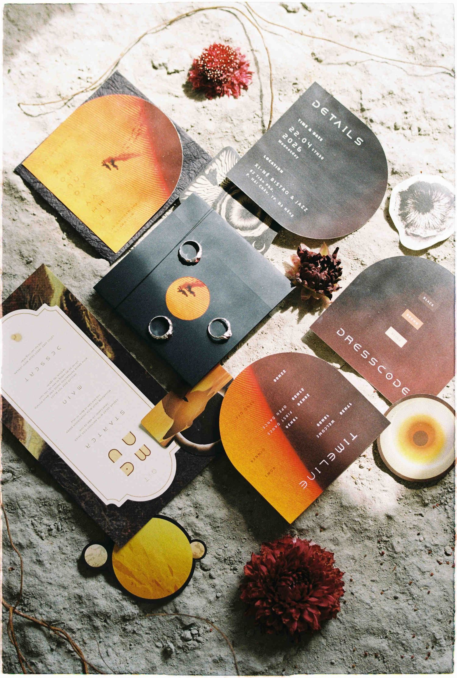 Artistic wedding stationery suite with warm sunset tones, featuring details, dresscode, and timeline cards arranged on sandy surface.