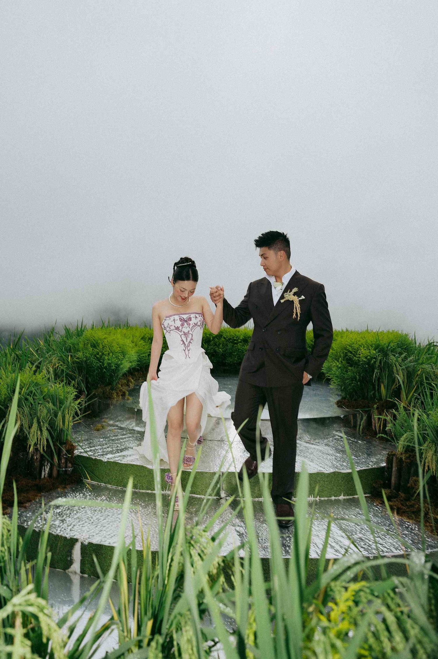 wedding: newlyweds share a tender moment near a water feature surrounded by lush greenery, by AnhVuWedding.