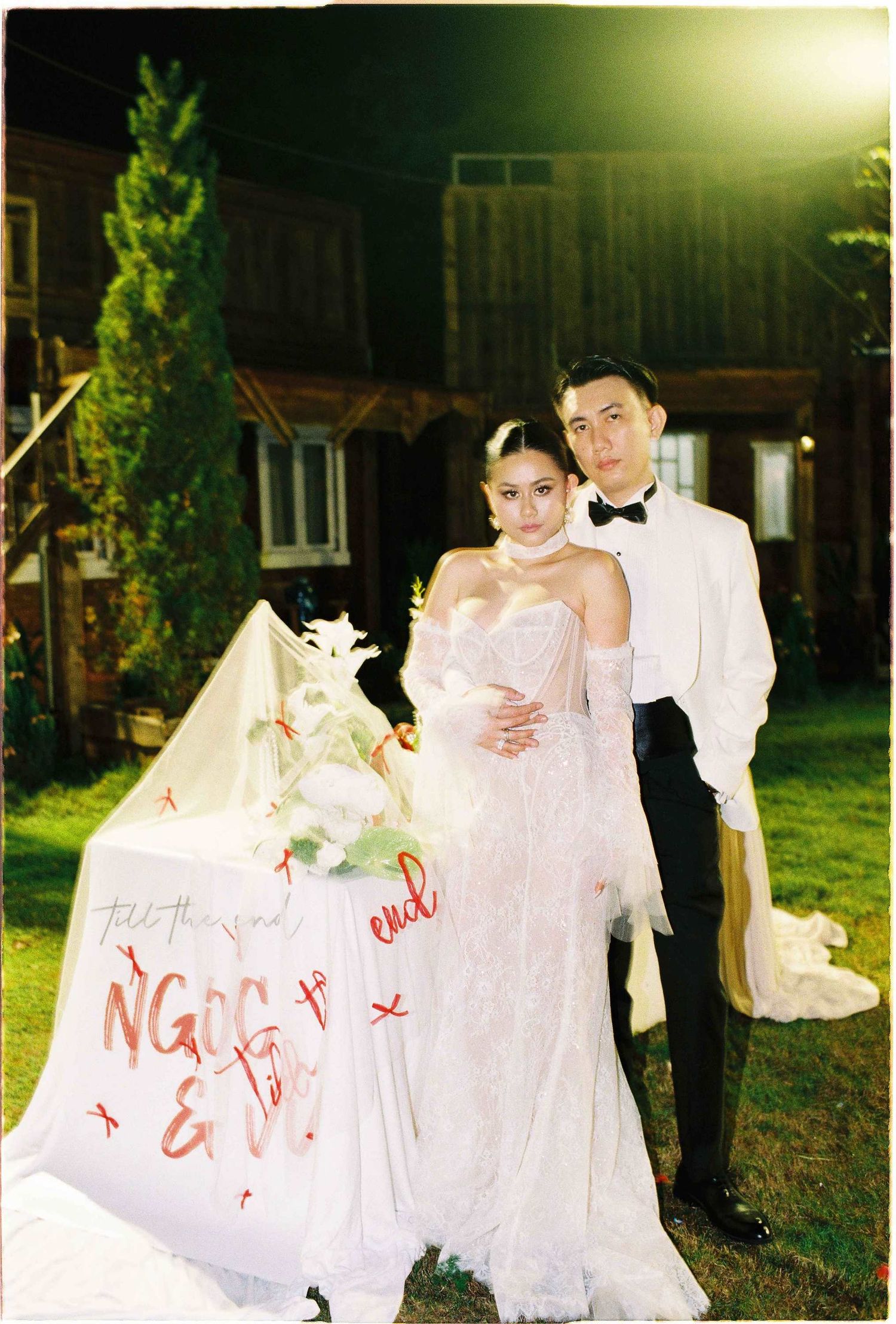 Saigon pre-wedding: wedding couple poses by a decorated table with white linens and floral arrangements in an outdoor, by AnhVuWedding.